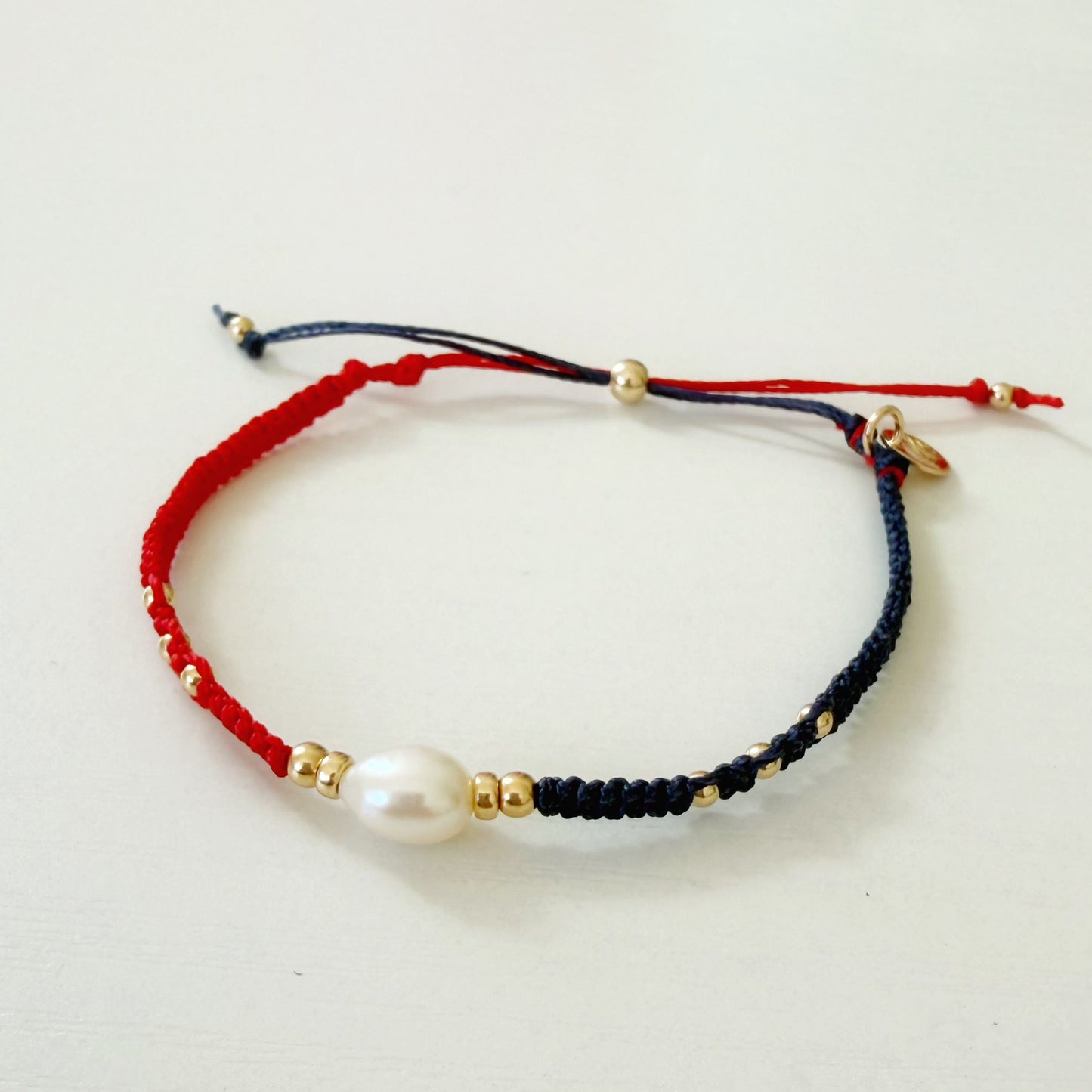 Bracelet with red, black, and gold cord and a pearl bead on a light gray background