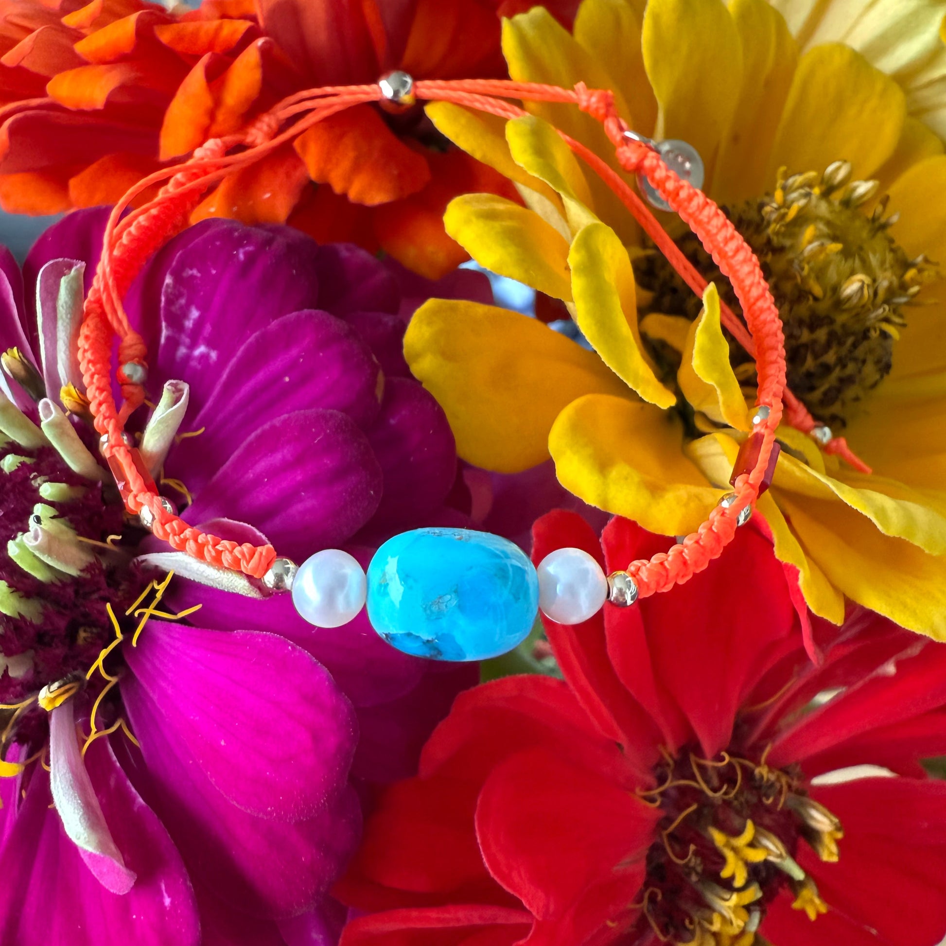 orange macramé adjustable bracelet with turquoise bead at the center with freshwater pearls. this bracelet is photographed on bright colored flowers