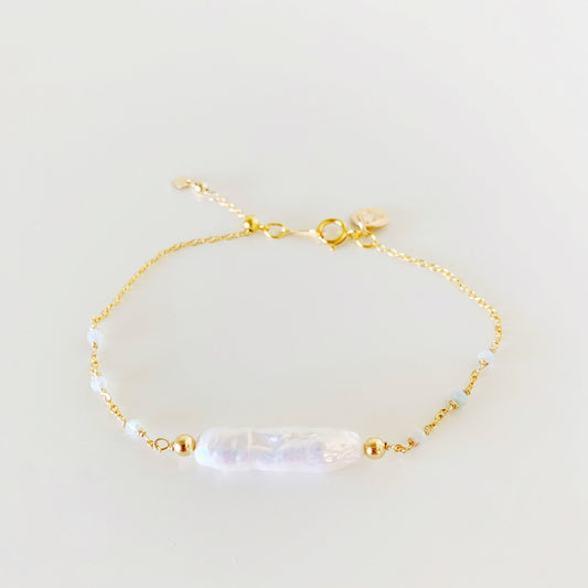 the truro adjustable bracelet by mermaids and madeleines is a chain based bracelet with a freshwater stick pearl at the center, with microfaceted aquamarine gems on the 14k gold filled chain on either side. the clasp has a slide bead to tighten the bracelet. this piece is photographed facing forward on a white surface