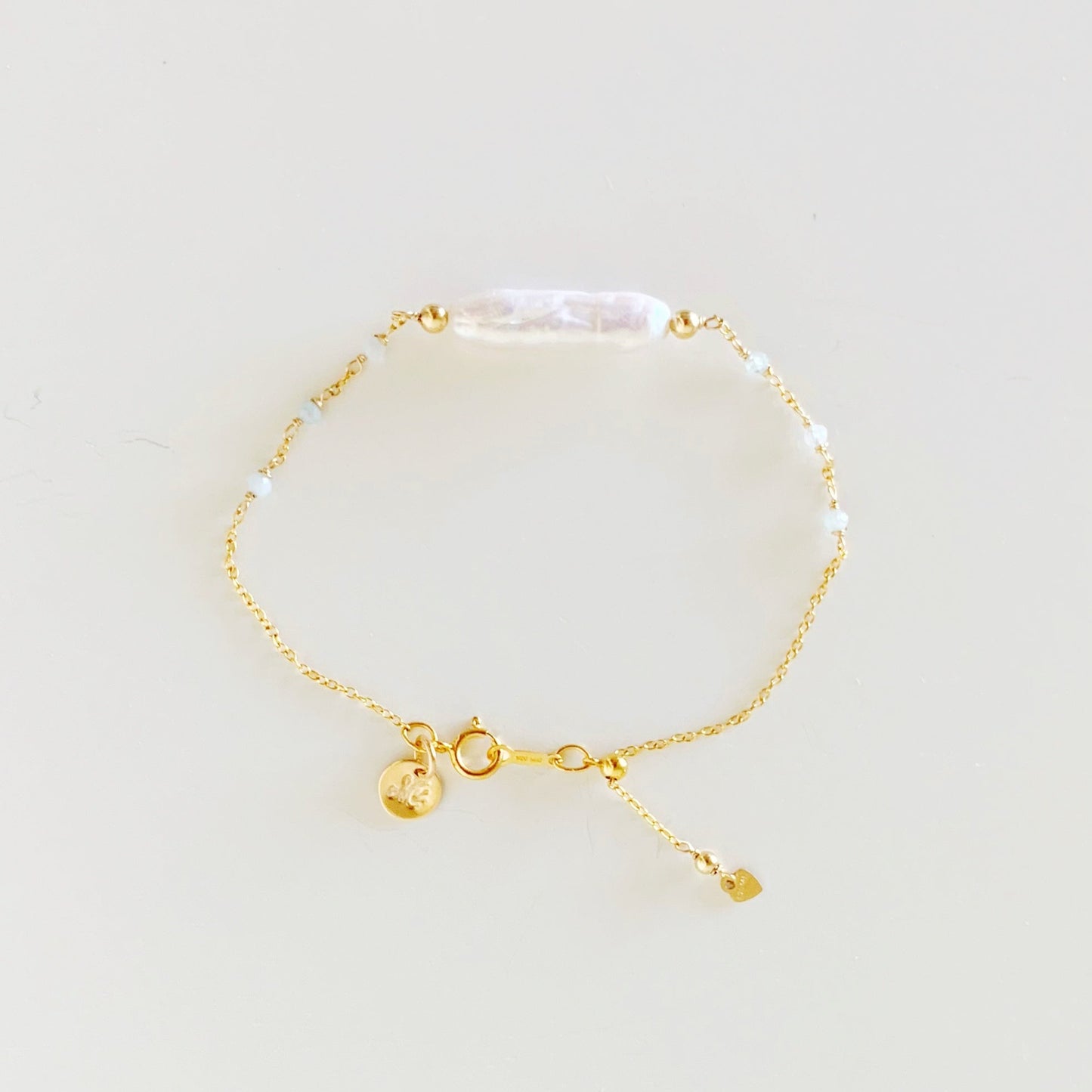 the truro bracelet by mermaids and madeleines is an adjustable chain based bracelet with freshwater stick pearl at the center and microfaceted aquamarine beads on the chain on either side. the chain and findings are 14k gold filled and there's a slide bead by the spring ring to tighten bracelet. this piece is photographed in a top down view on a white surface