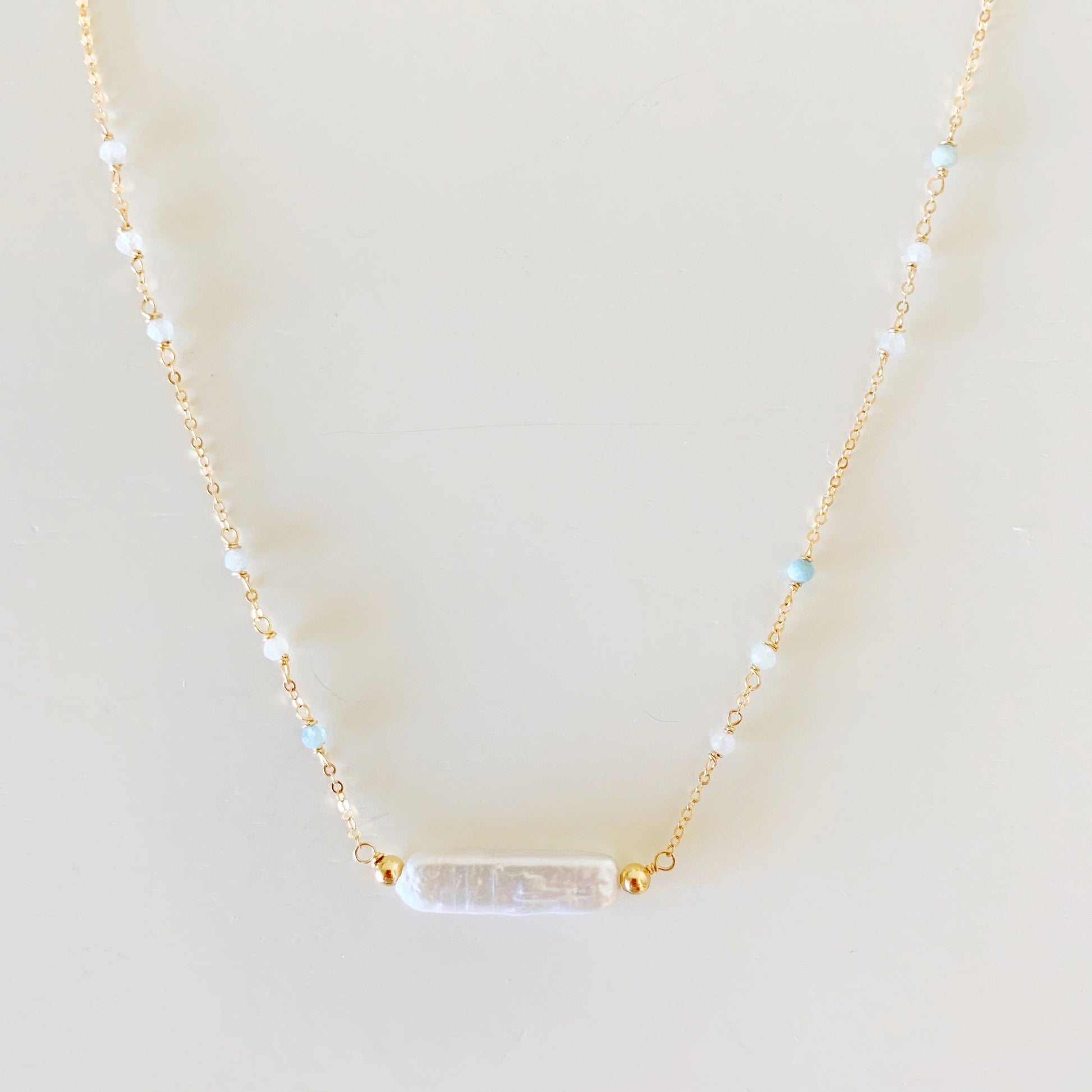 The truro necklace is designed with 14k gold filled chain and findings and a freshwater stick pearl at the center with  microfaceted aquamarine along the chain up the necklace. this necklace is photographed closer up on a white surface