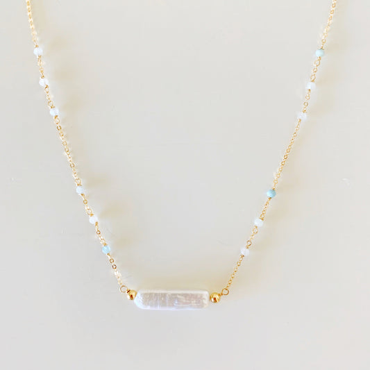 The truro necklace is designed with 14k gold filled chain and findings and a freshwater stick pearl at the center with  microfaceted aquamarine along the chain up the necklace. this necklace is photographed closer up on a white surface