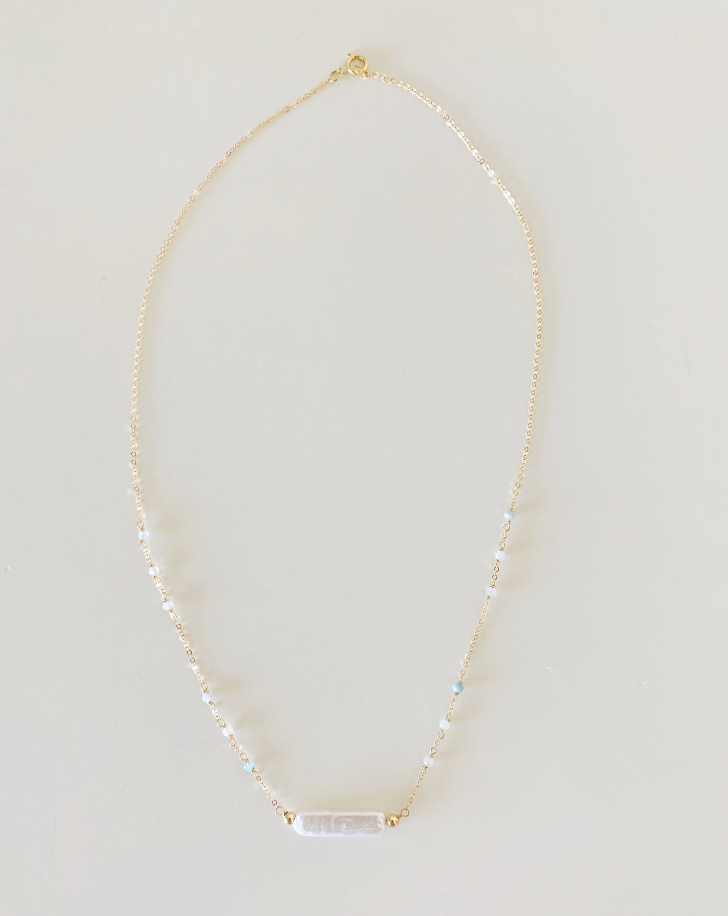 the truro necklace by mermaids and madeleines is created with 14k gold filled chain dotted with microfaceted aquamarine beads with a freshwater stick pearl at the center. this is a full length view of the necklace photographed on a white background