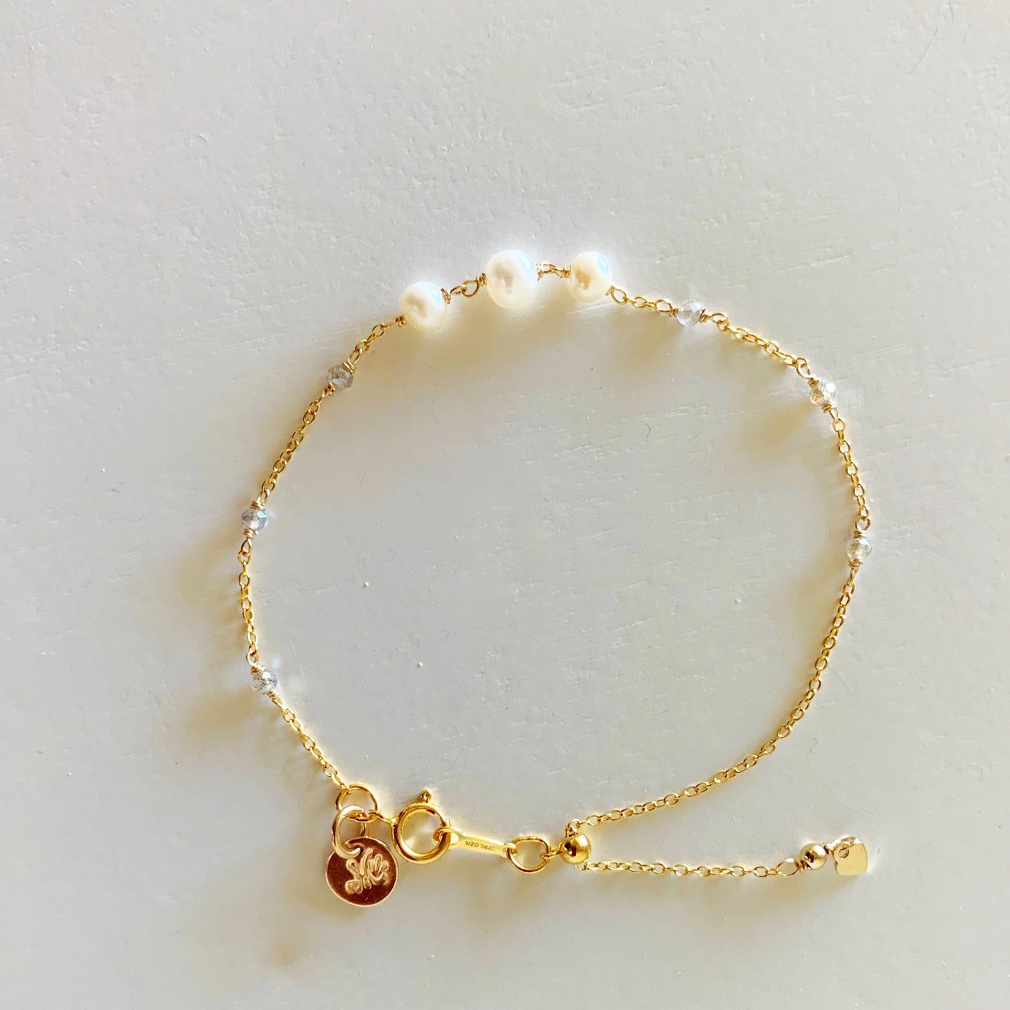 the westport bracelet by mermaids and madeleines is an adjustable style bracelet created with 14k gold filled chain and 3 freshwater pearls at the center of the bracelet with tiny microfaceted labradorite beads on the sides of the chain. this bracelet is photographed in full view from the top down on a white surface