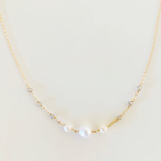 the westport necklace by mermaids and madeleines is a 14k gold filled chain necklace with three freshwater white pearls wire wrapped at the center and tiny microfaceted labradorite beads on the sides. this necklace has a close up view and is photographed on a white surface