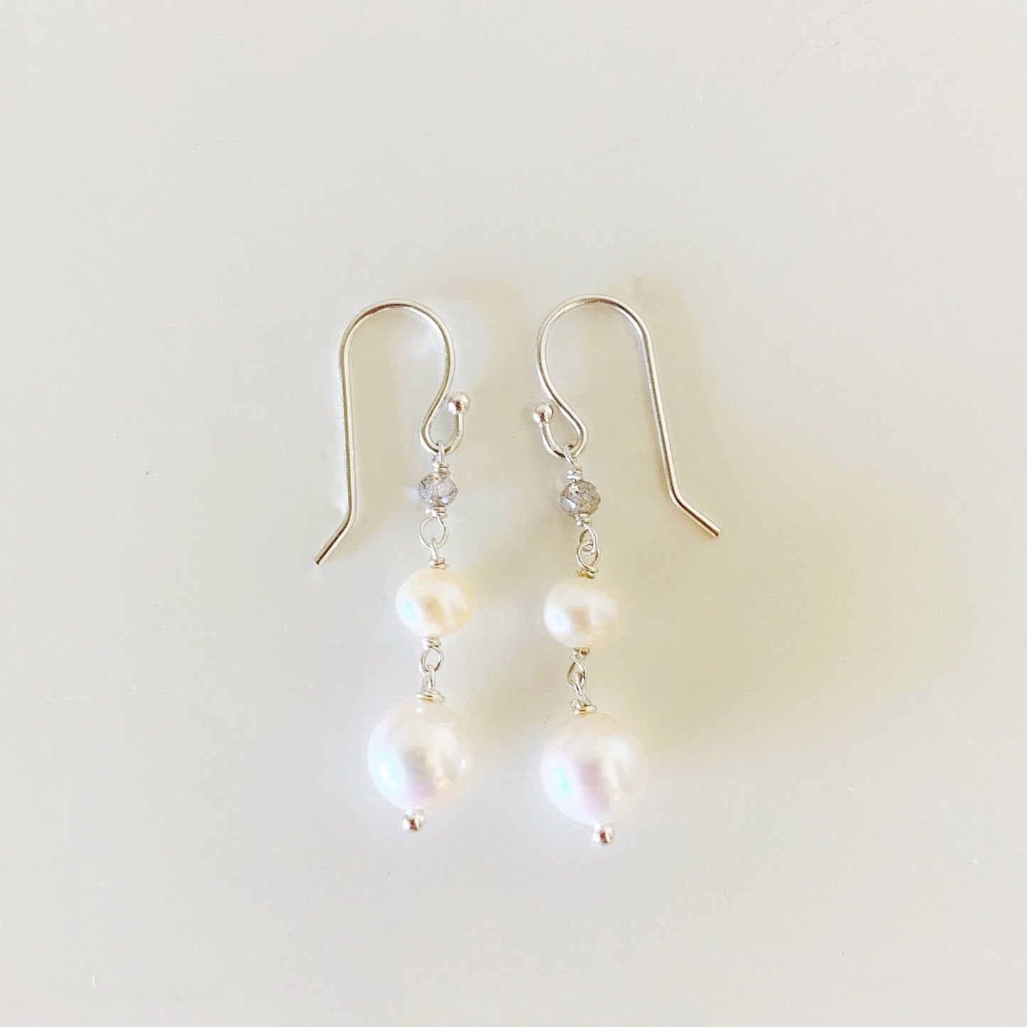 The westport earrings by mermaids and madeleines are created with freshwater pearl and labradorite gems. A simple dangling earring with sterling silver findings. This pair of earrings is photographed on a white surface