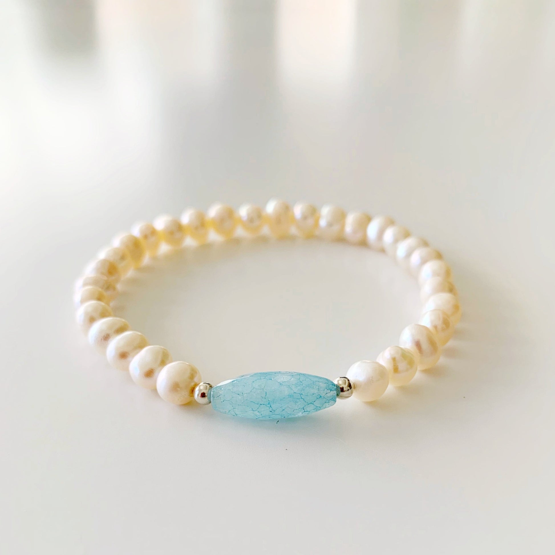 you're a gem stretch bracelet by mermaids and madeleines is designed with an aquamarine gem in the center with sterling silver beads and freshwater pearls. this bracelet is photographed on a white surface
