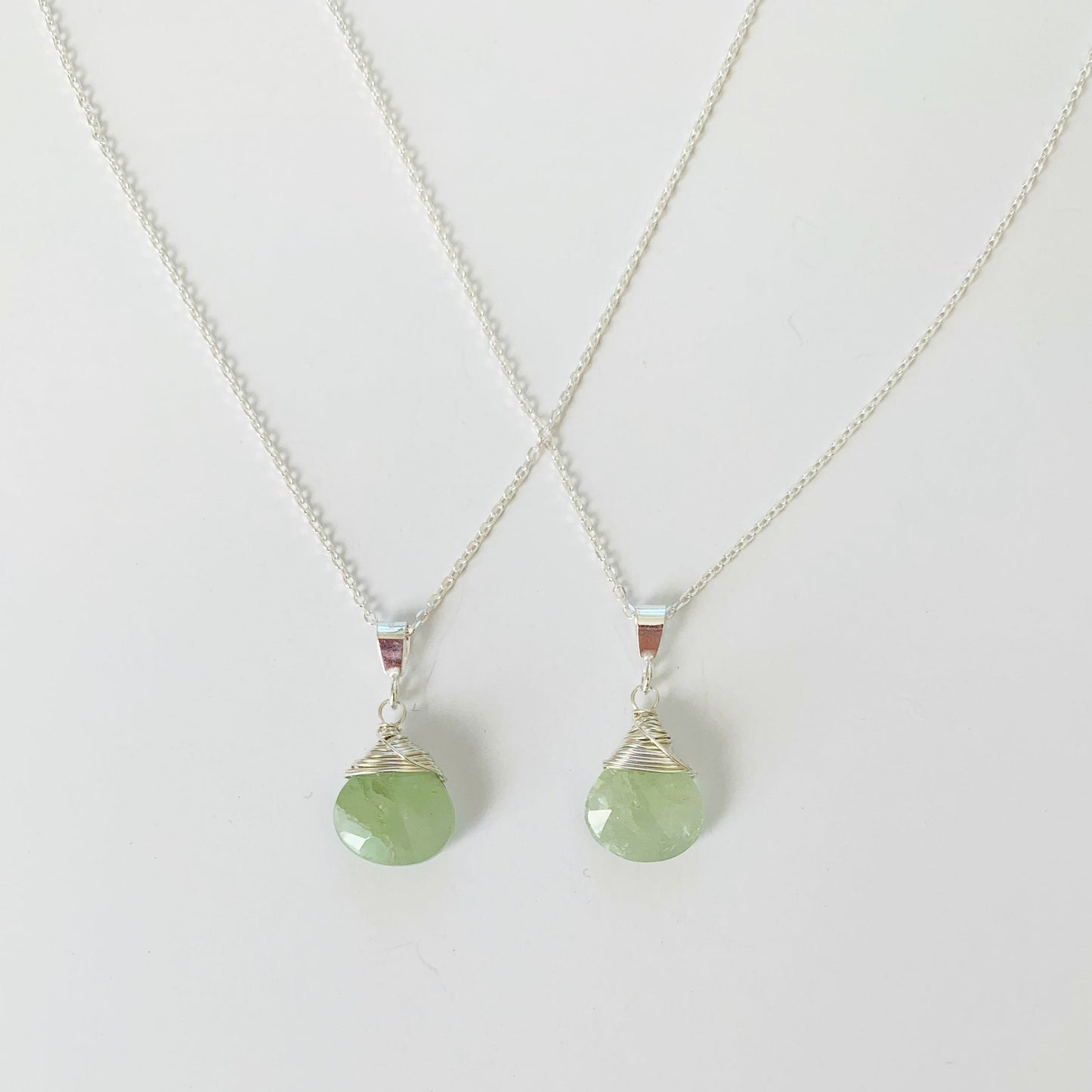 2 raindrop wire wrapped necklaces in sterling silver and aquamarine pictured on a white surface