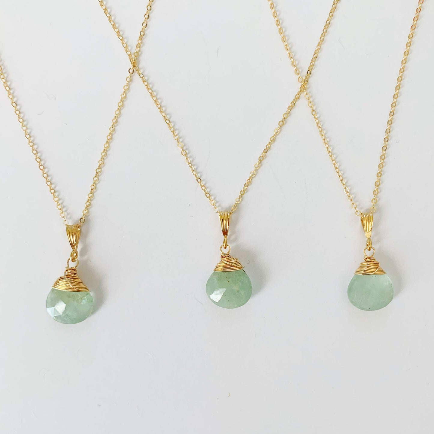 a photograph of 3 mermaids and madeleines raindrop necklaces created from aquamarine briolettes and 14k gold filled wire, chain and findings photographed on a white surface