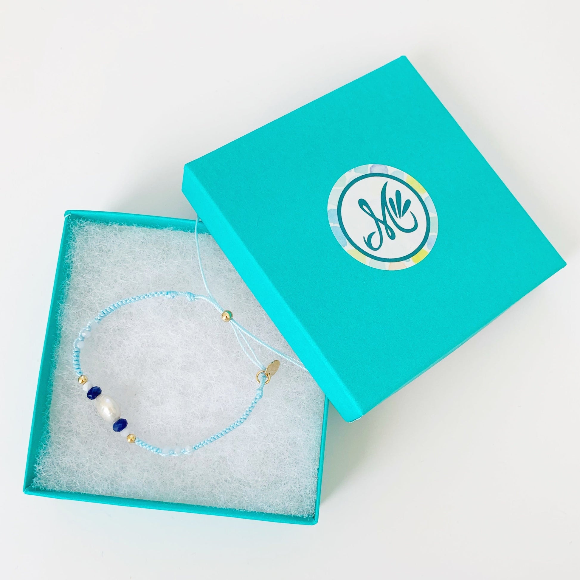 forget me knot light blue macrame bracelet photographed in a teal mermaids and madeleines box on a white surface