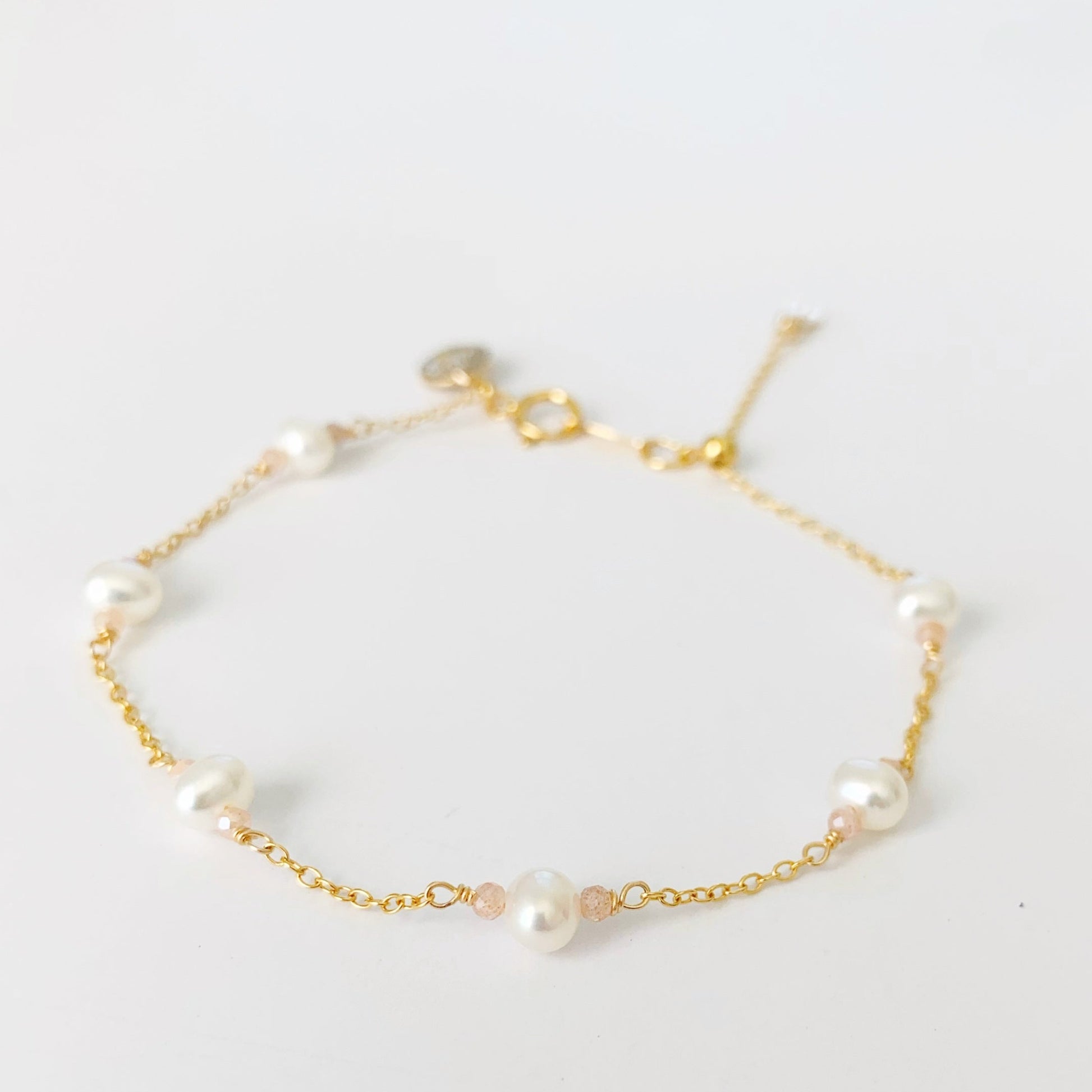The barrington bracelet by mermaids and madeleines is a station tin-cup style bracelet created with freshwater pearls and peach moonstone beads on 14k gold filled chain, the bracelet has a spring ring clasp and adjustable slide bead closure. this bracelet is photographed on a white background