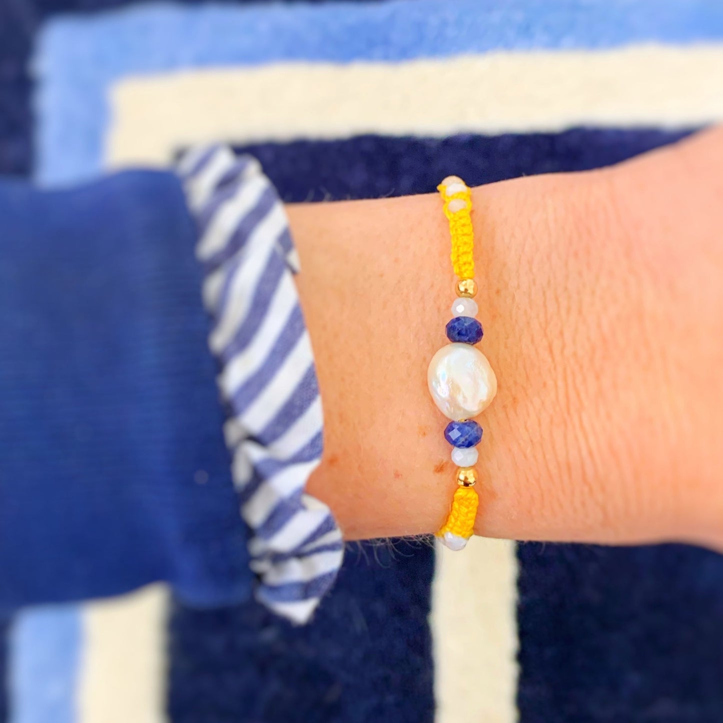 A photo of the bristol buttercup macrame yellow adjustable friendship bracelet worn on a wrist over a navy blue backdrop