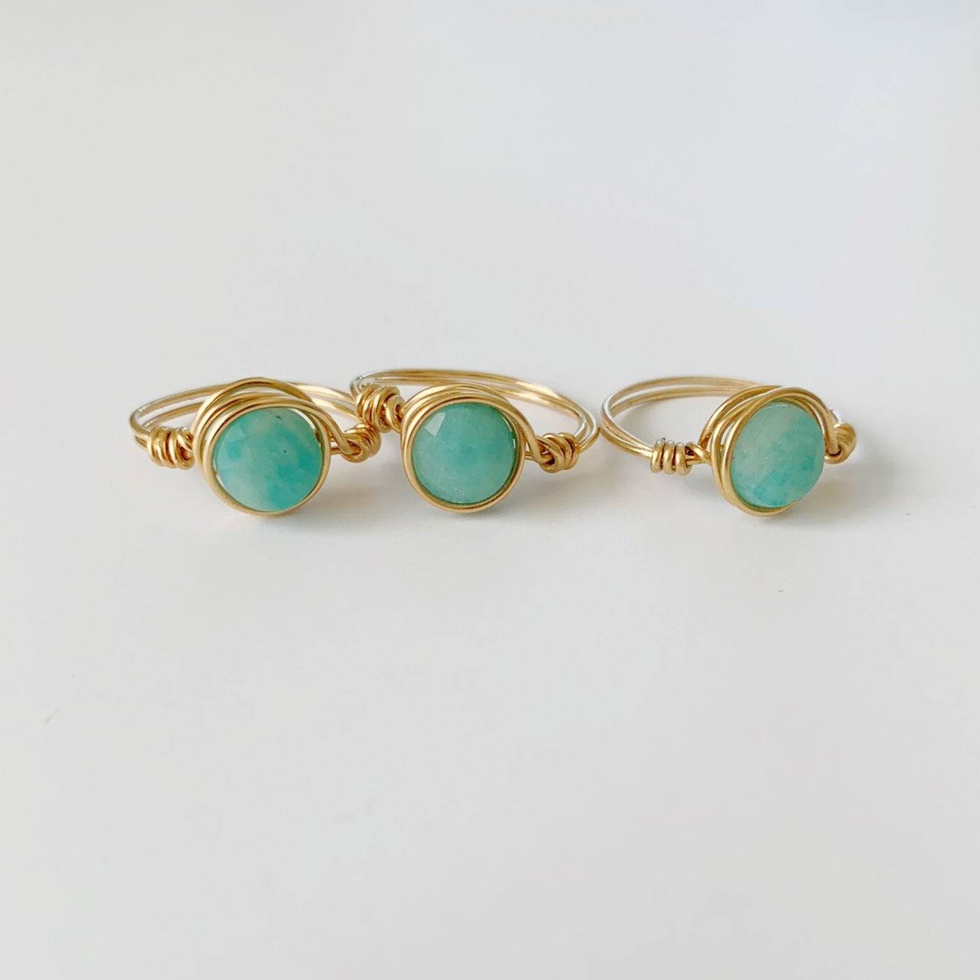 A photo of 3 captiva rings by mermaids and madeleines photographed on a white surface. The rings are 14k gold filled wire wrapped with amazonite gems