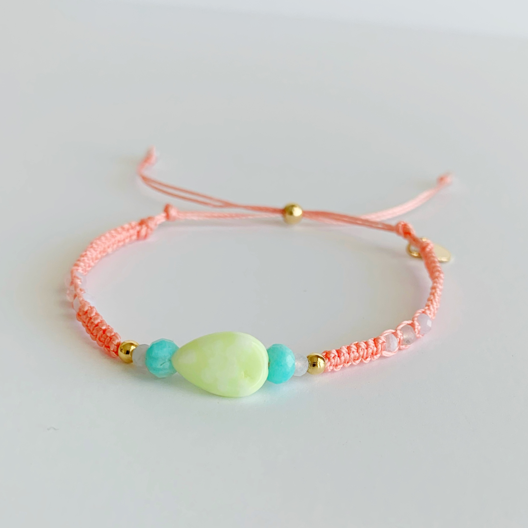 Peach color macramé cord bracelet with teardrop shaped lime jade bead and bright aqua amazonite beads at the center of the bracelet on a white background