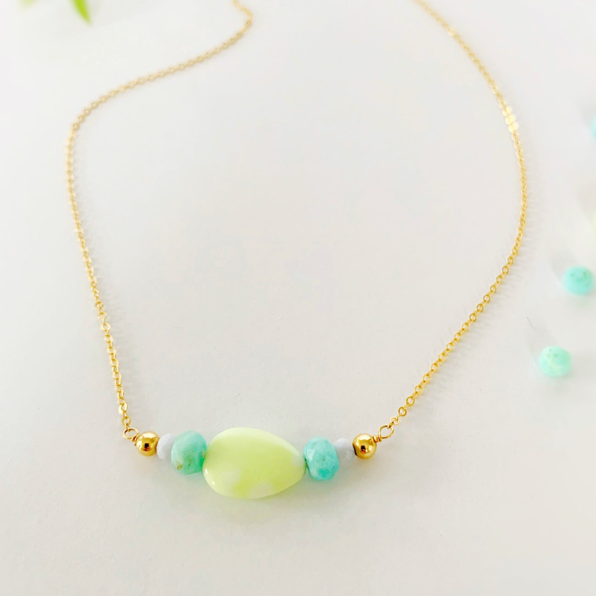 The captiva necklace is designed with 14k gold filled chain with a center segment of beads including a teardrop shaped lime jade, with amazonite and blue lace agate faceted rondelles on either side. This necklace is photographed flat on a white surface