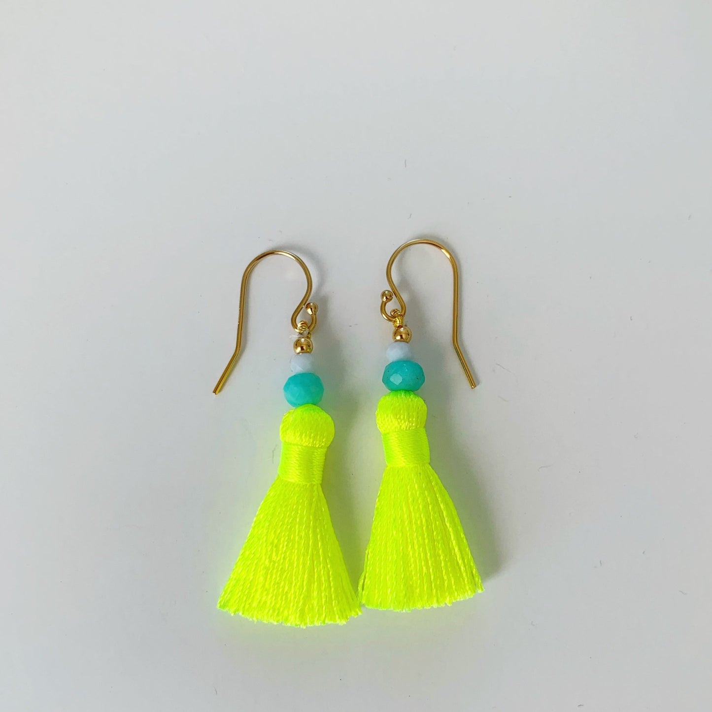 Captiva Tassel earrings by mermaids and madeleines are neon yellow tassels with amazonite, blue lace agate and 14k gold filled findings. this pair is pictured on a white surface