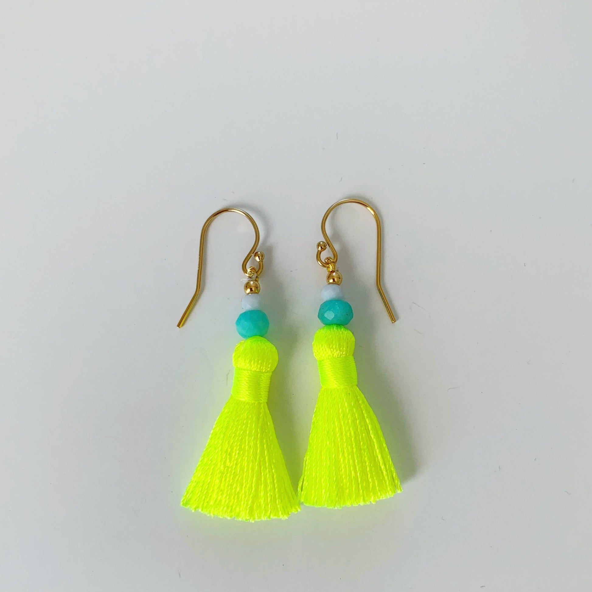 Captiva Tassel earrings by mermaids and madeleines are neon yellow tassels with amazonite, blue lace agate and 14k gold filled findings. this pair is pictured on a white surface