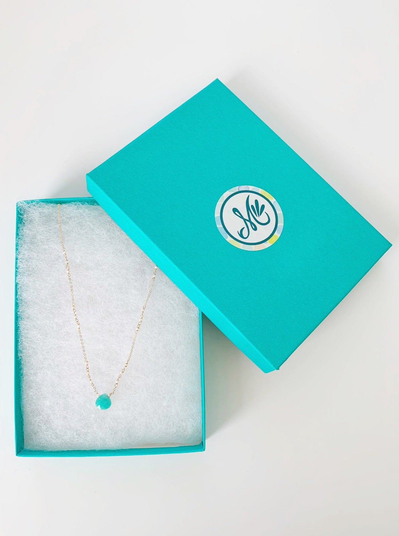 Island Air necklace by mermaids and madeleines pictured here in a white cotton lined teal gift box. The necklace is created with a bright amazonite gem at the center with tiny freshwater pearls on 14k gold filled chain