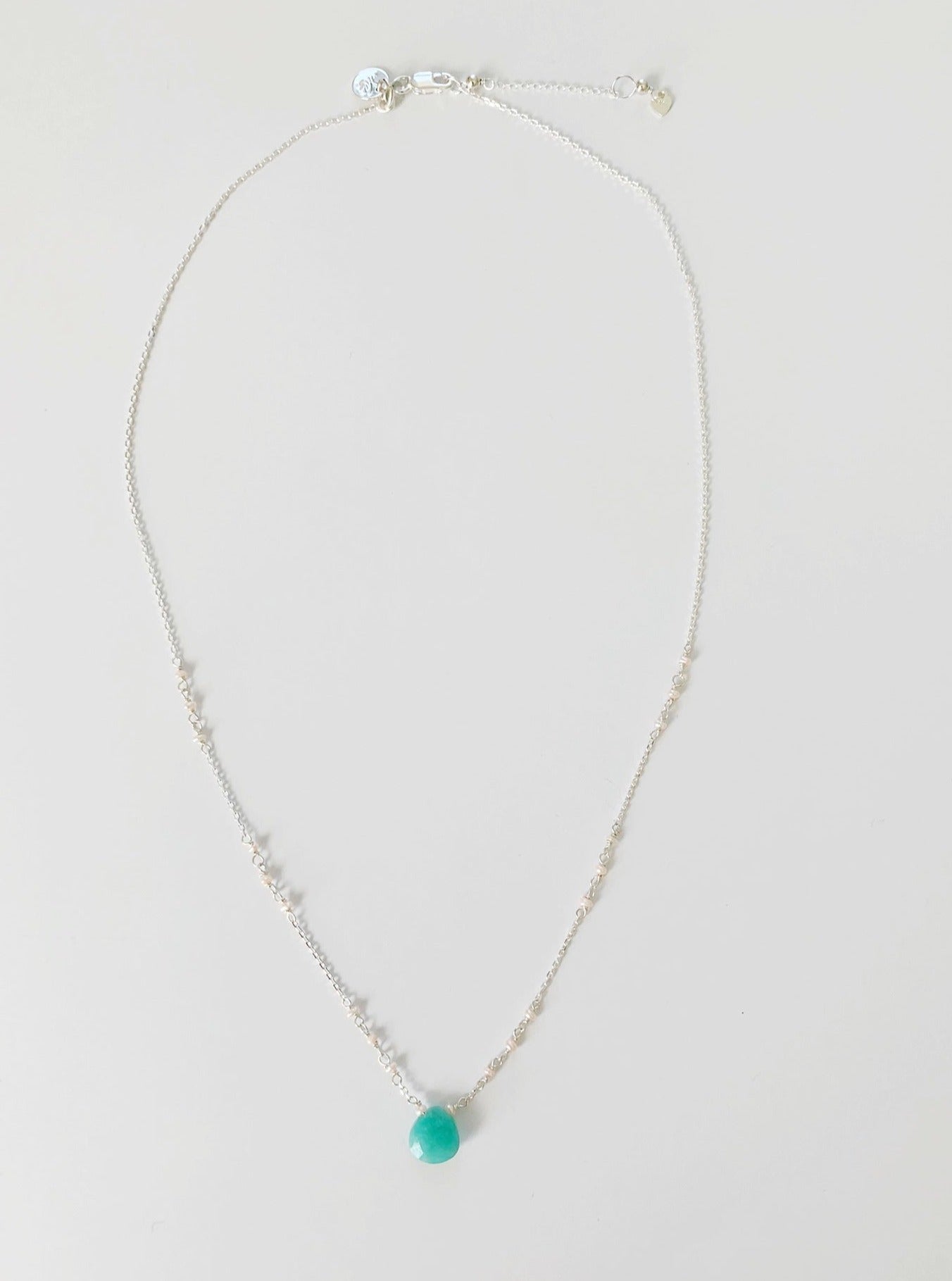 A full length view of the Island Air necklace by Mermaids and Madeleines. The necklace features a bright aqua briolette at the center and freshwater pearls wired into the sterling silver chain. This necklace is photographed on a white background