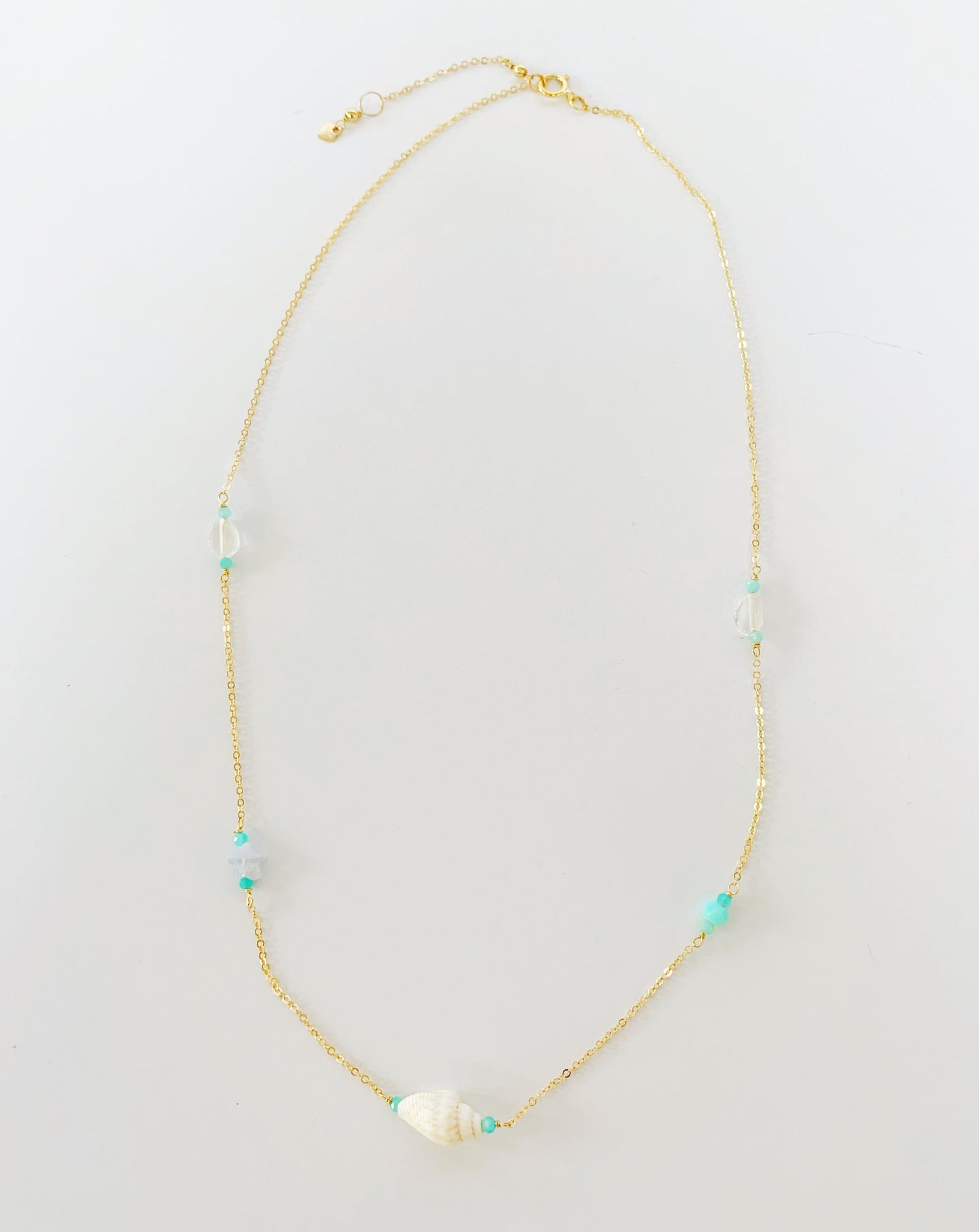 The island hopper necklace is a station necklace with 5 stations, a shell at center and then semiprecious stones for the remaining 4 including rose quartz, peruvian opal, blue lace agate, amazonite. clasped at the 17" length. The necklace is photographed flat on a white background