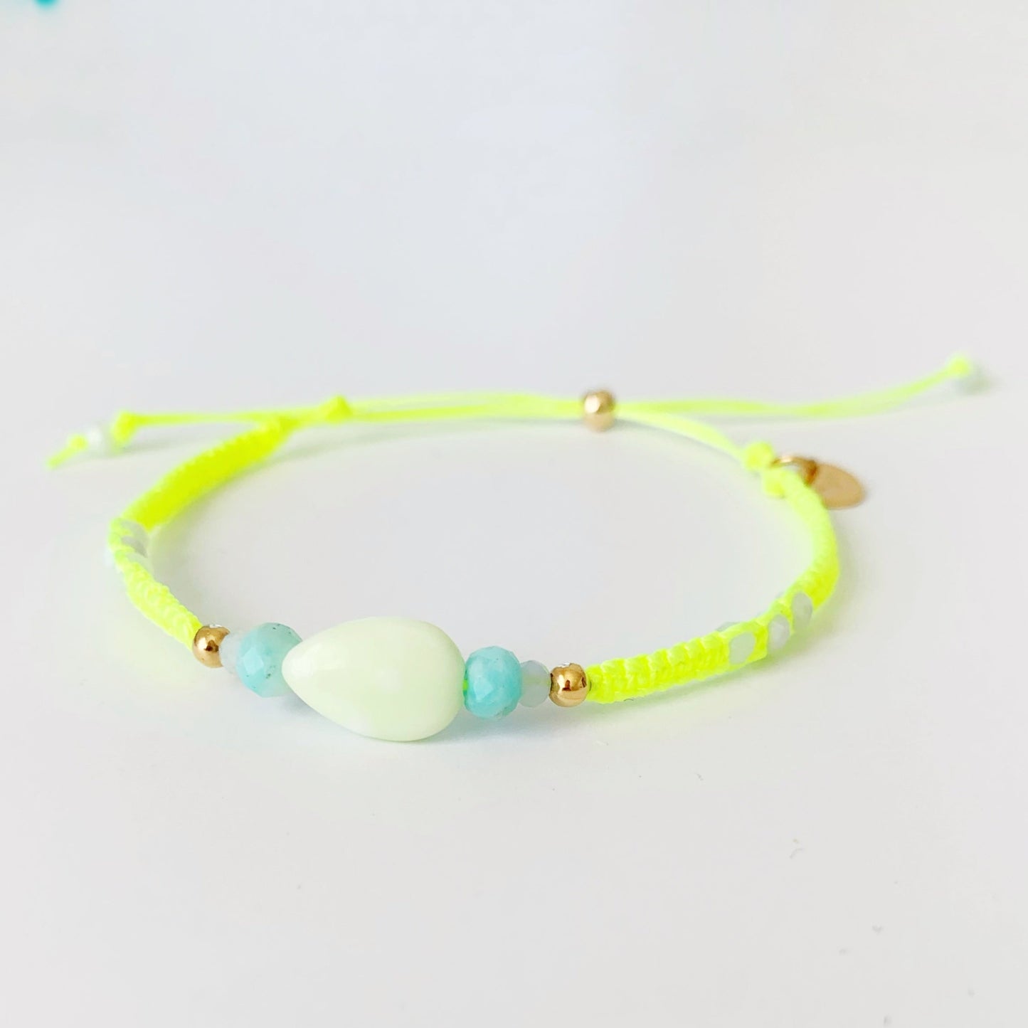 the mermaids and madeleines captiva macrame bracelet in color sips on the court is a neon yellow cord friendship bracelet with semiprecious beads at the center and a 14k gold filled slide clasp. this one is photographed on a white surface