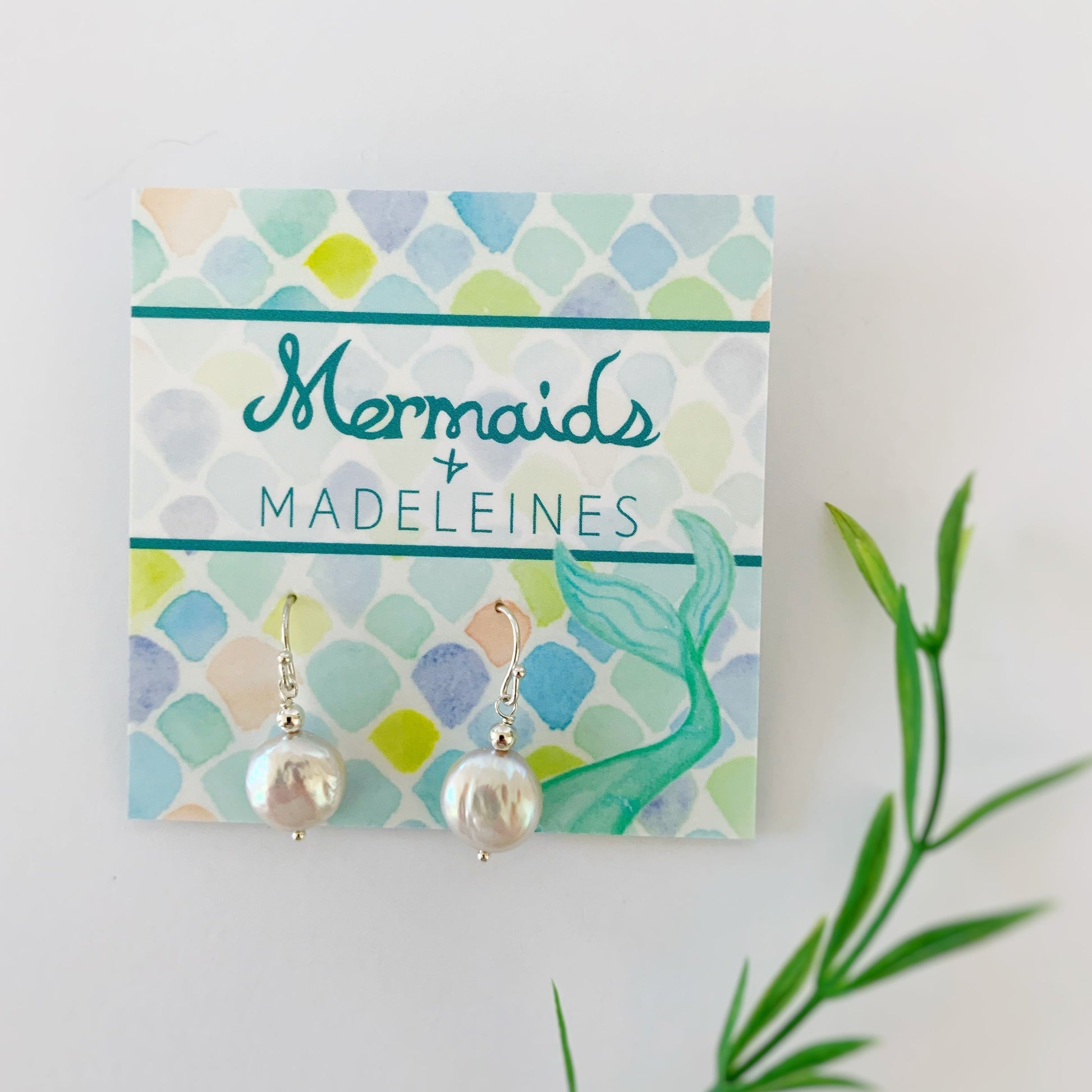 Newport earrings in sterling. This pair of earrings is created with sterling silver beads and earring findings with iridescent freshwater coin pearls. This pair is photographed on a mermaids and madeleines earring card and photographed on a white background with a little bit of blurred greenery in the bottom right corner