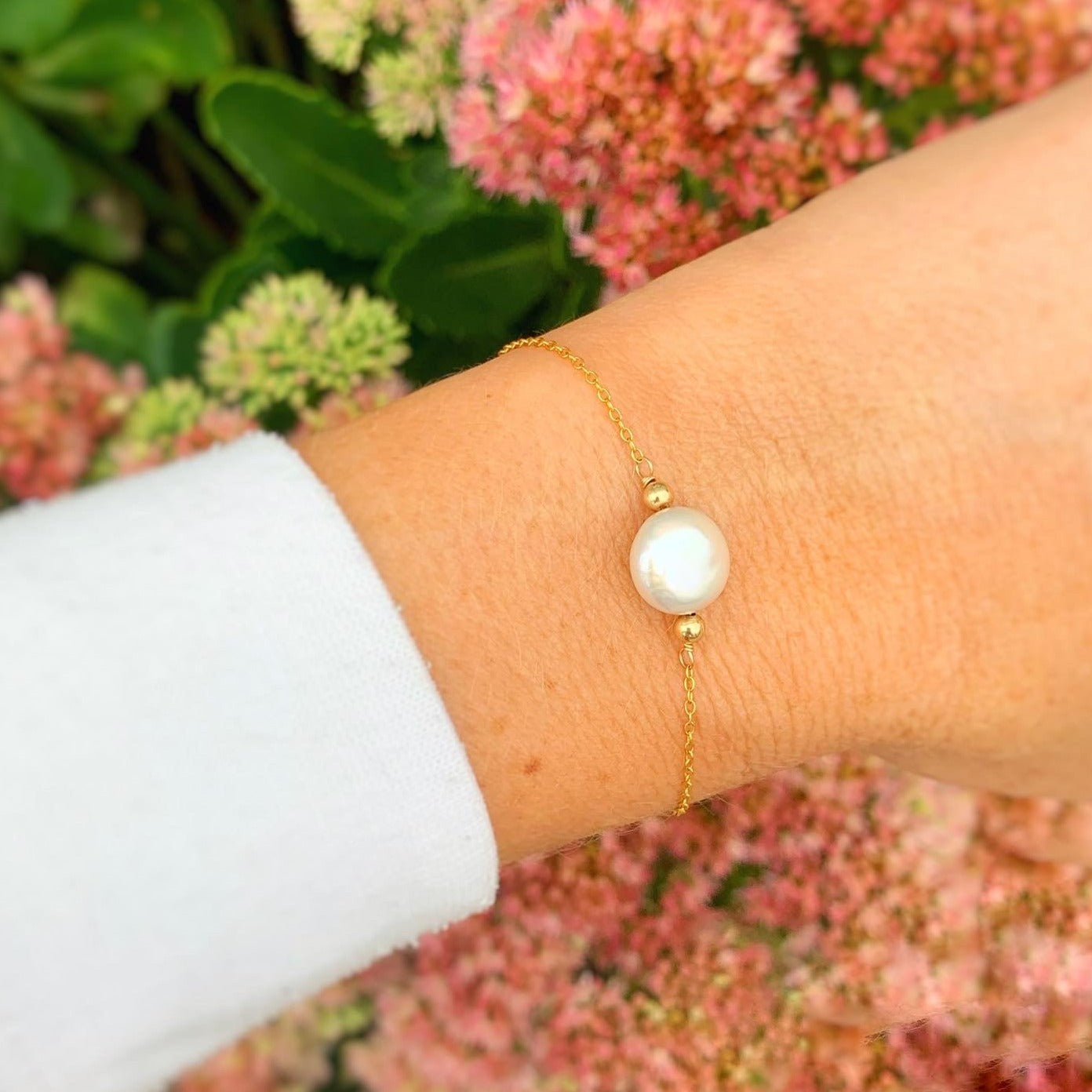 Newport coin pearl bracelet by Mermaids and Madeleines features a freshwater coin pearl and 14k gold filled beads, chain and findings. This bracelet is pictured on a wrist with a blurred pink flower in the background