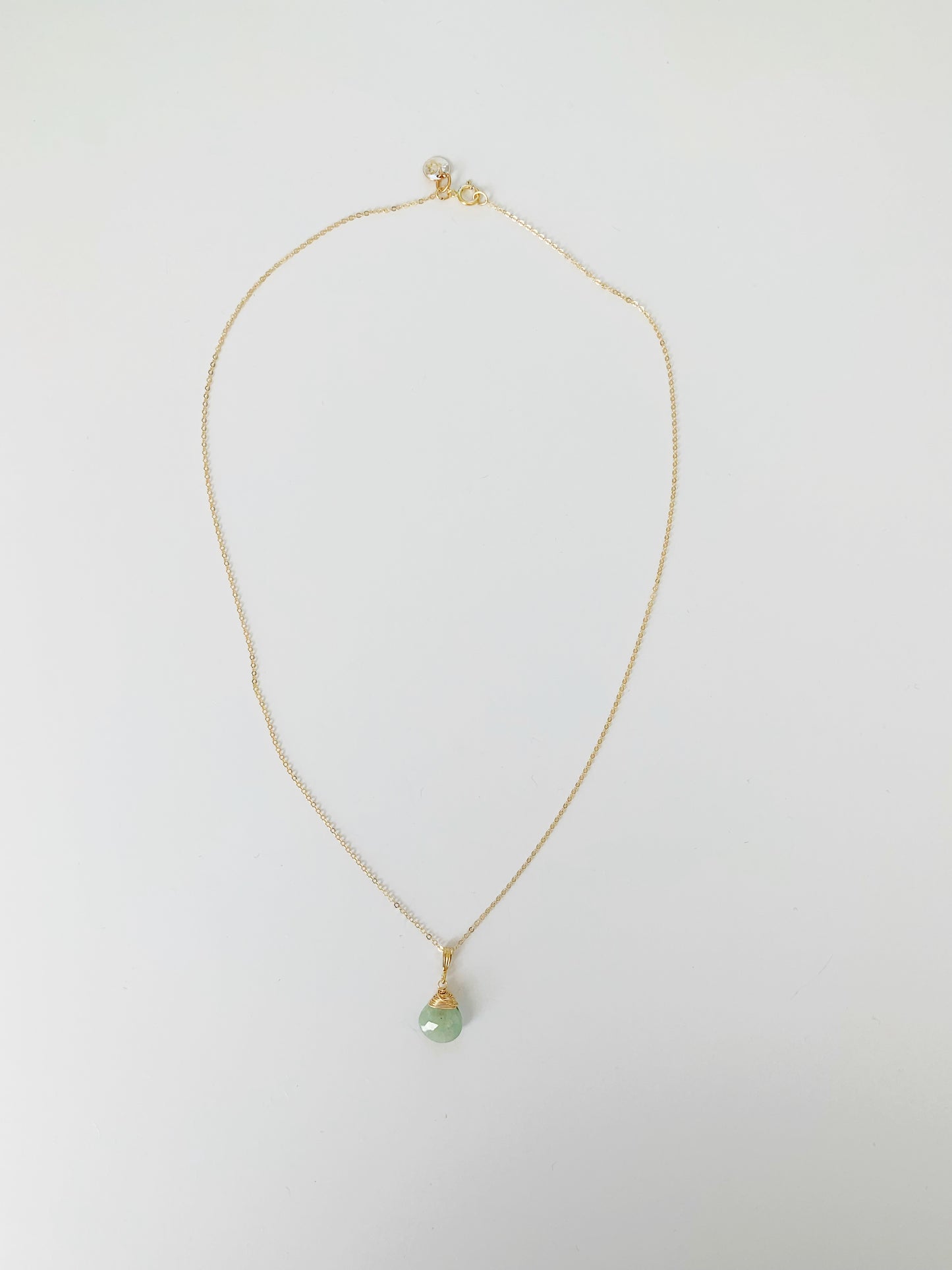 A full length view of the raindrop necklace in 14k gold filled with aquamarine wire wrapped pendant on a white surface