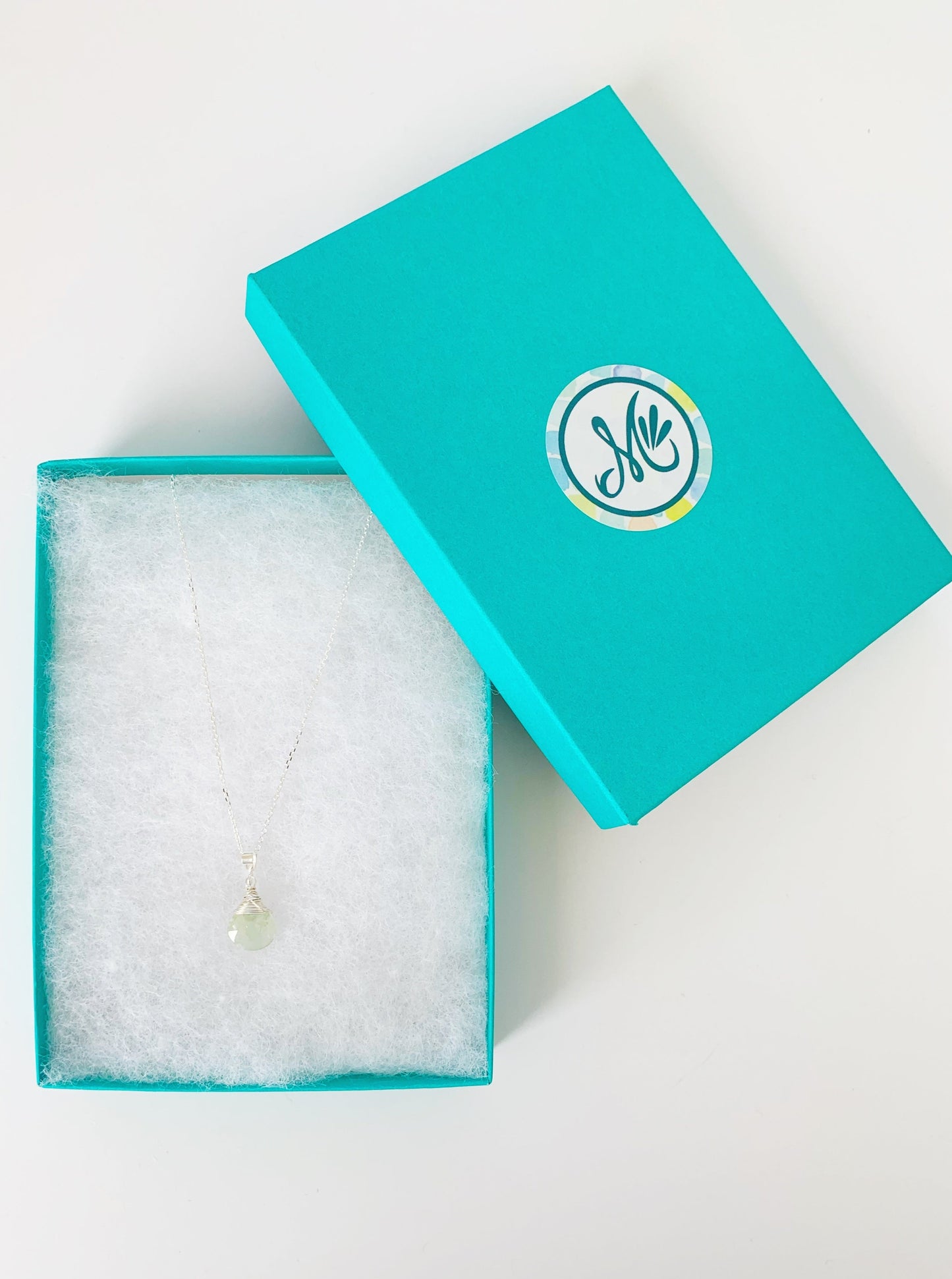 Raindrop aquamarine and sterling silver wire wrapped pendant necklace pictured in a teal gift box on a white surface