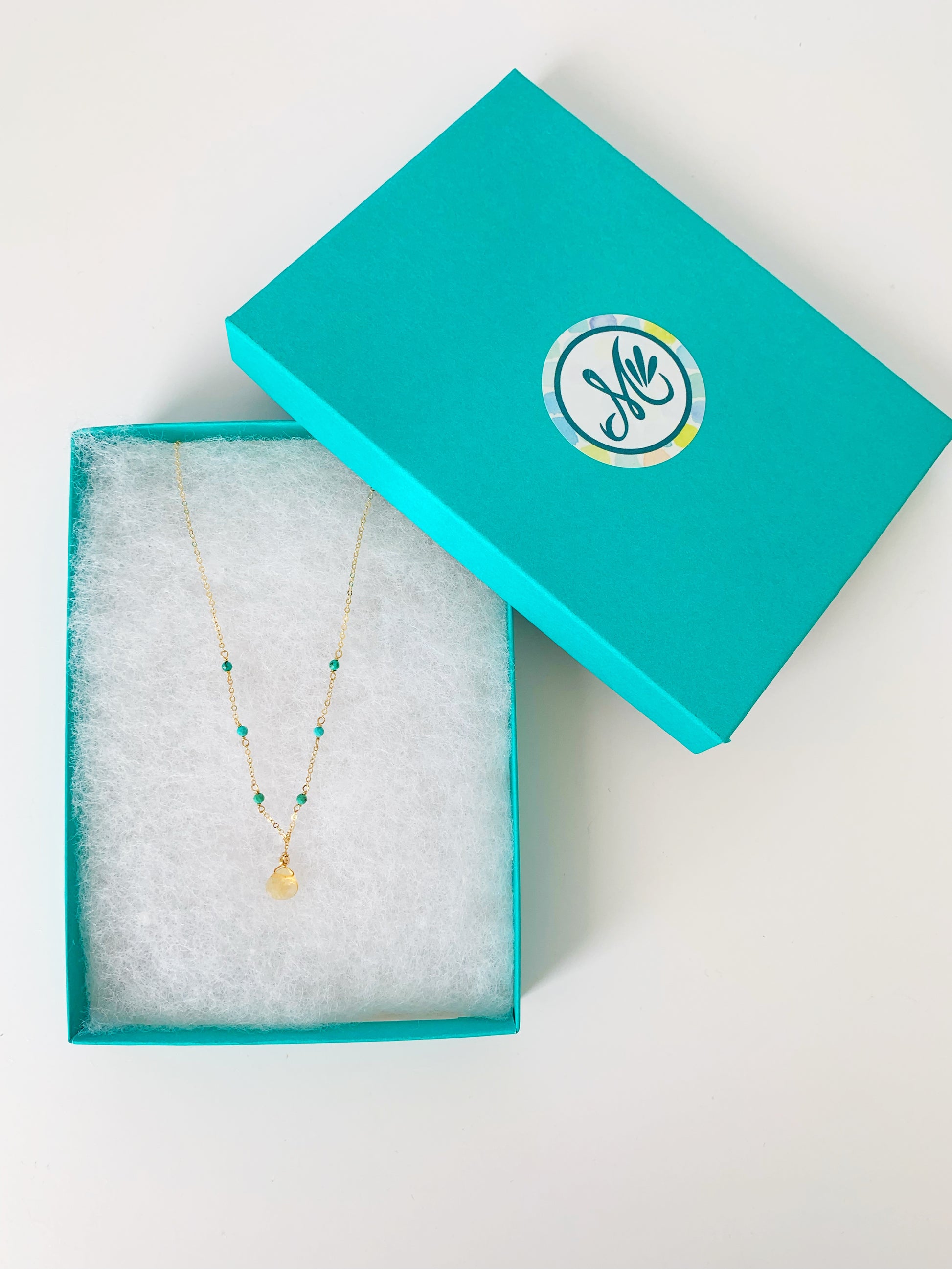 the ray of sunshine necklace photographed in a teal gift box on a white surface