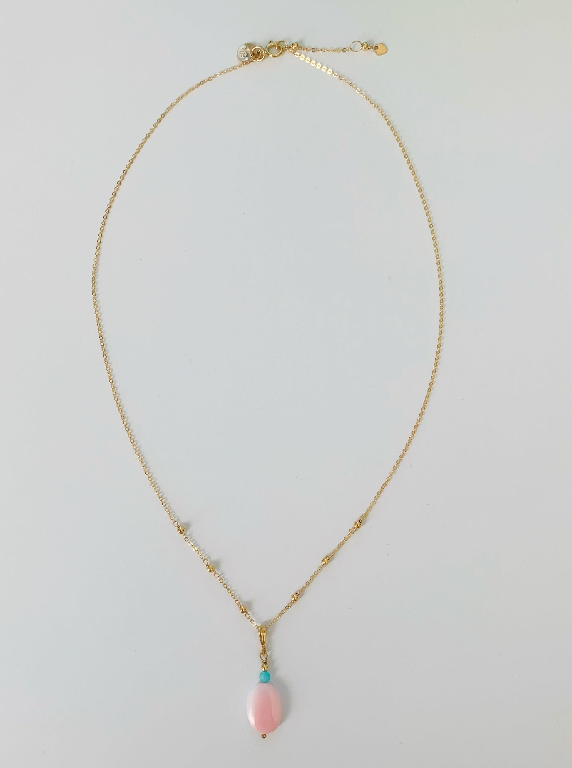 Full length view of the sanibel necklace. necklace has a pink conch shell bead as a pendant with an amazonite bead and its on 14k gold filled chain. this necklace is pictured on a white surface