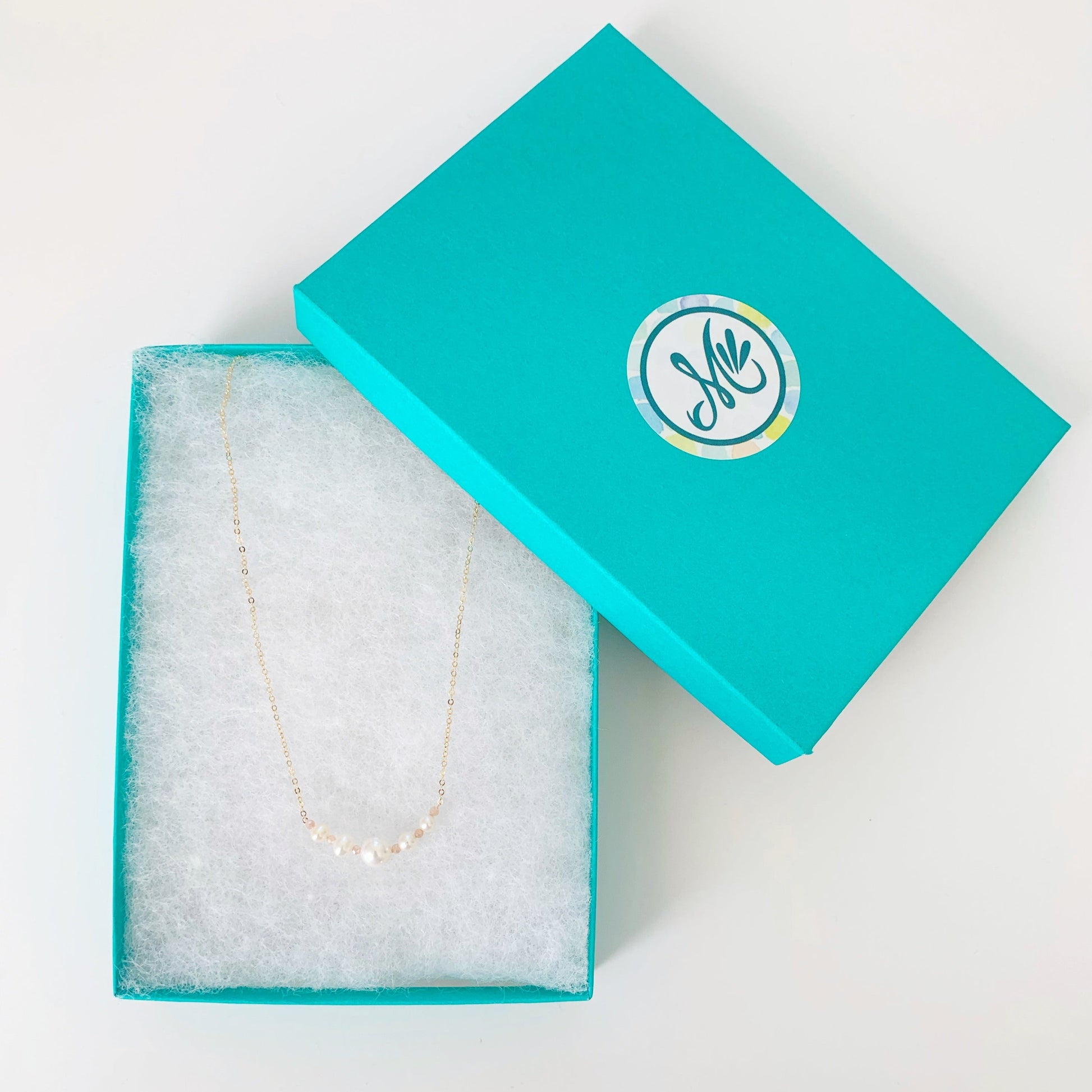 The barrington freshwater pearl and peach moonstone necklace with 14k gold filled chain and findings pictured in a teal gift box on a white surface