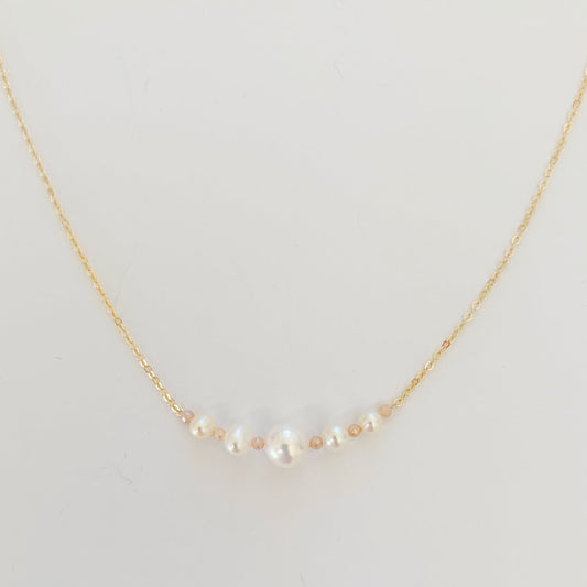 The barrington necklace by mermaids and madeleines has graduated freshwater pearls at the center with peach moonstone on 14k gold filled chain. this necklace is photographed close up and on a white surface