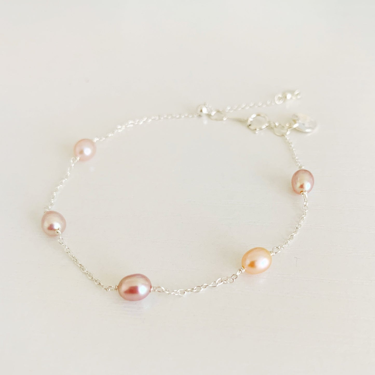 block island bracelet by mermaid and madeleines features natural pink color, small oval pearls in stations on sterling silver chain. There's a slide bead near the clasp to adjust. the bracelet is photographed on a white surface