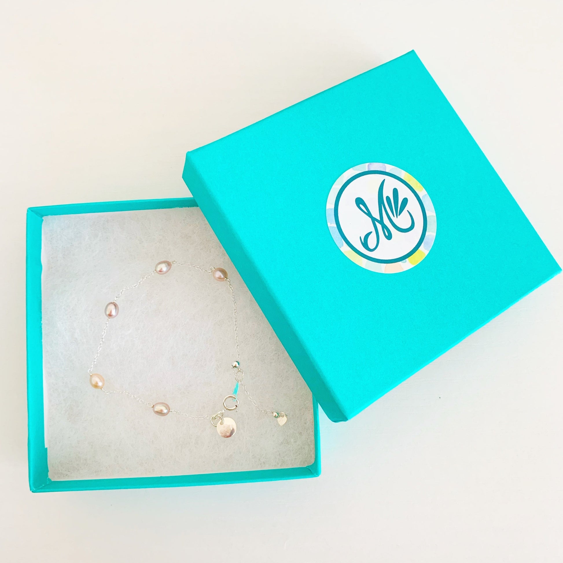 block island adjustable bracelet by mermaids and madeleines features natural pink color small oval pearls in stations on a sterling silver chain bracelet. theres a slide bead to adjust the length near the clasp. this bracelet is photographed in a cotton lined teal gift box on a white surface
