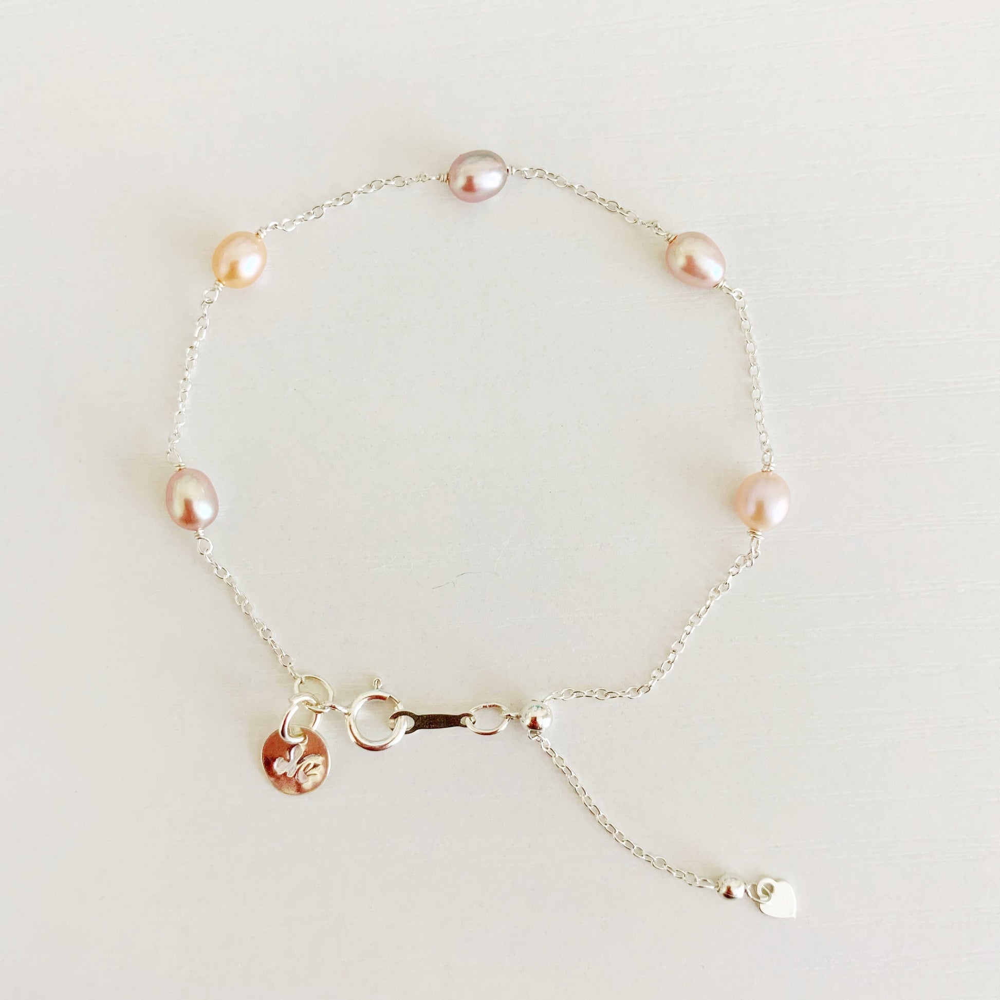 Block Island bracelet by mermaids and madeleines features natural pink color freshwater pearls in stations on a sterling silver chain bracelet. theres a slide bead near the clasp to adjust length. this bracelet is photographed in full view on a white surface