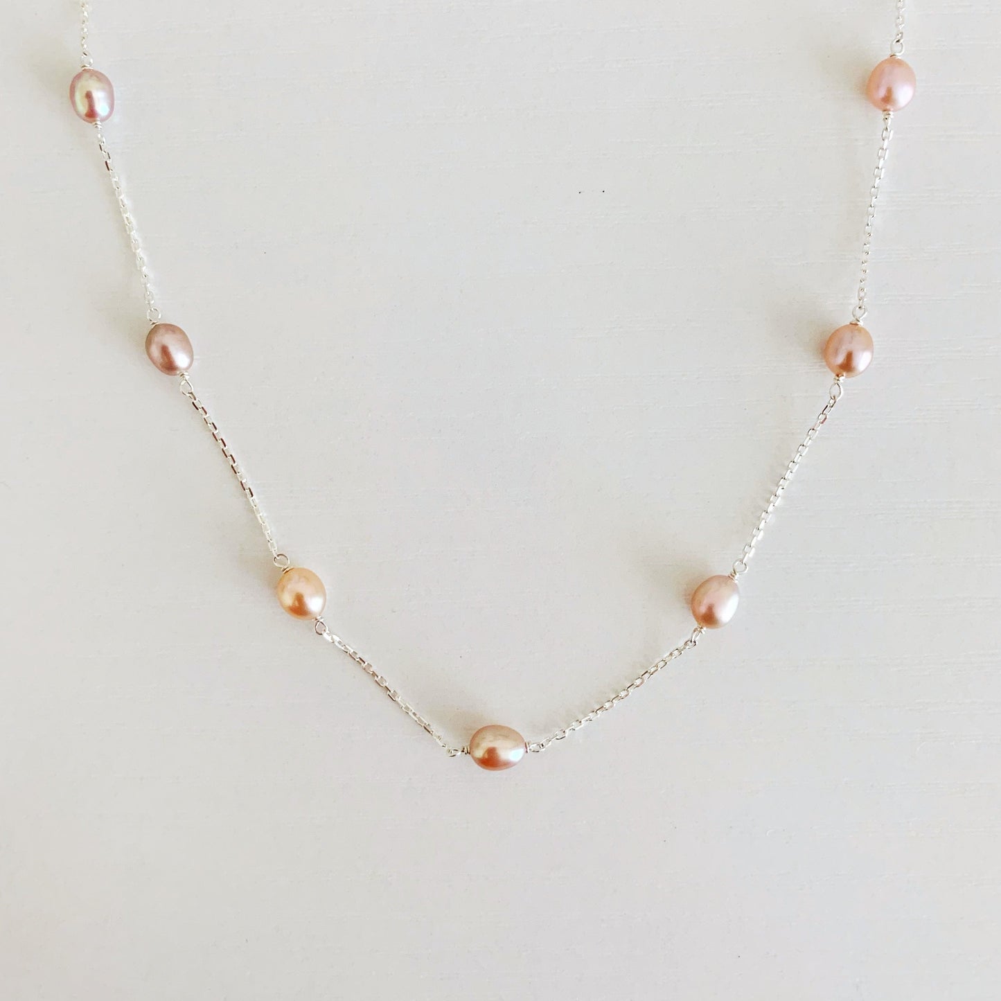 Block Island Necklace by mermaids and madeleines features pink natural color freshwater oval pearls in stations on sterling silver chain. this is a photo of just the front half of the necklace on a white surface