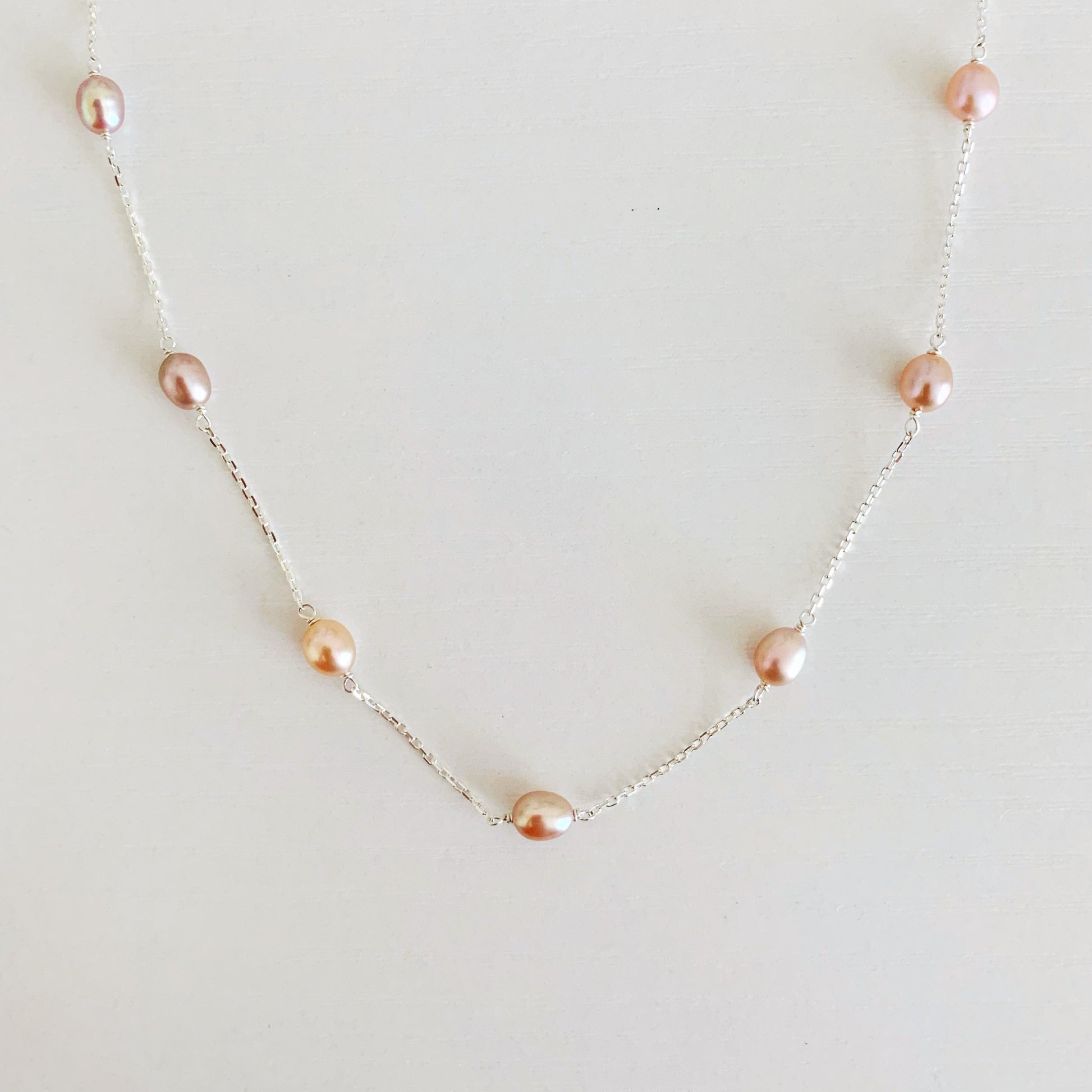 Block Island Necklace by mermaids and madeleines features pink natural color freshwater oval pearls in stations on sterling silver chain. this is a photo of just the front half of the necklace on a white surface