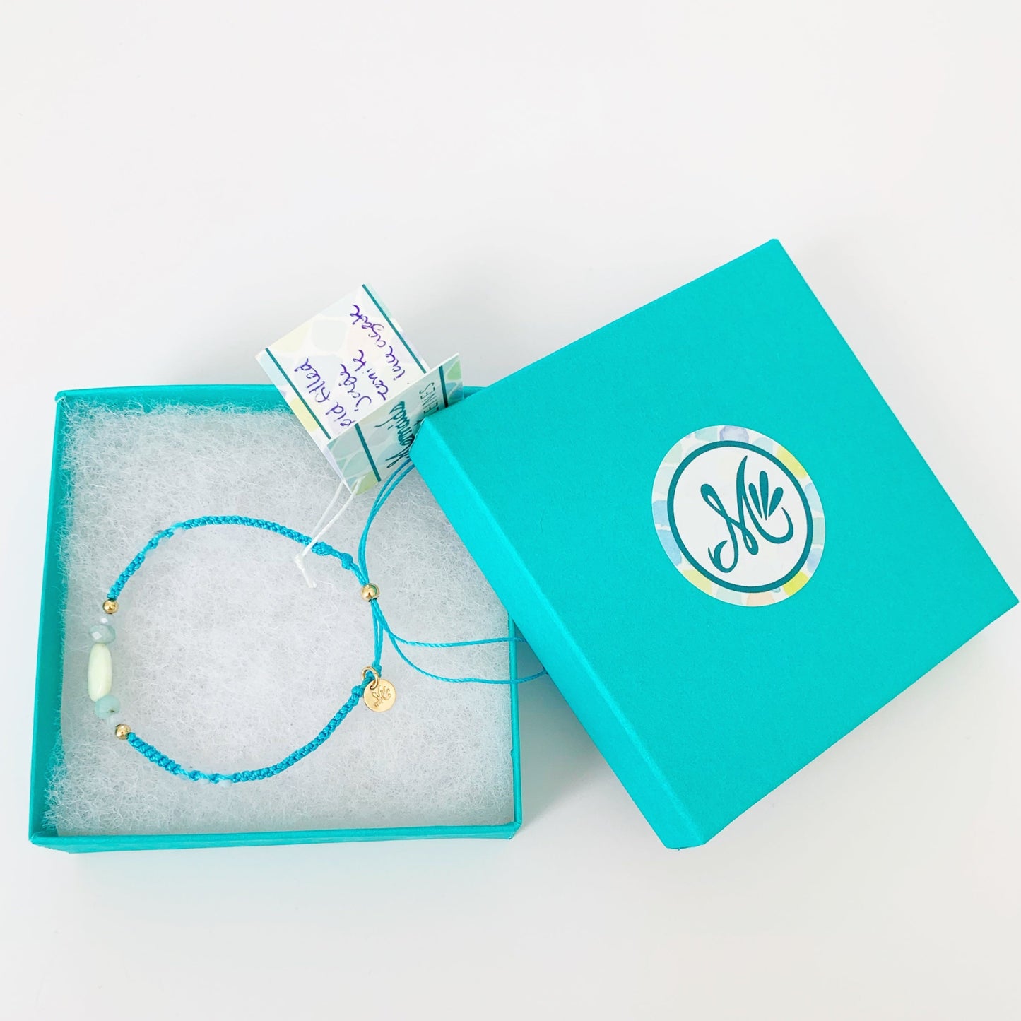 The captiva macrame bracelet in color blue crush pictured in a teal gift box on top of a white surface