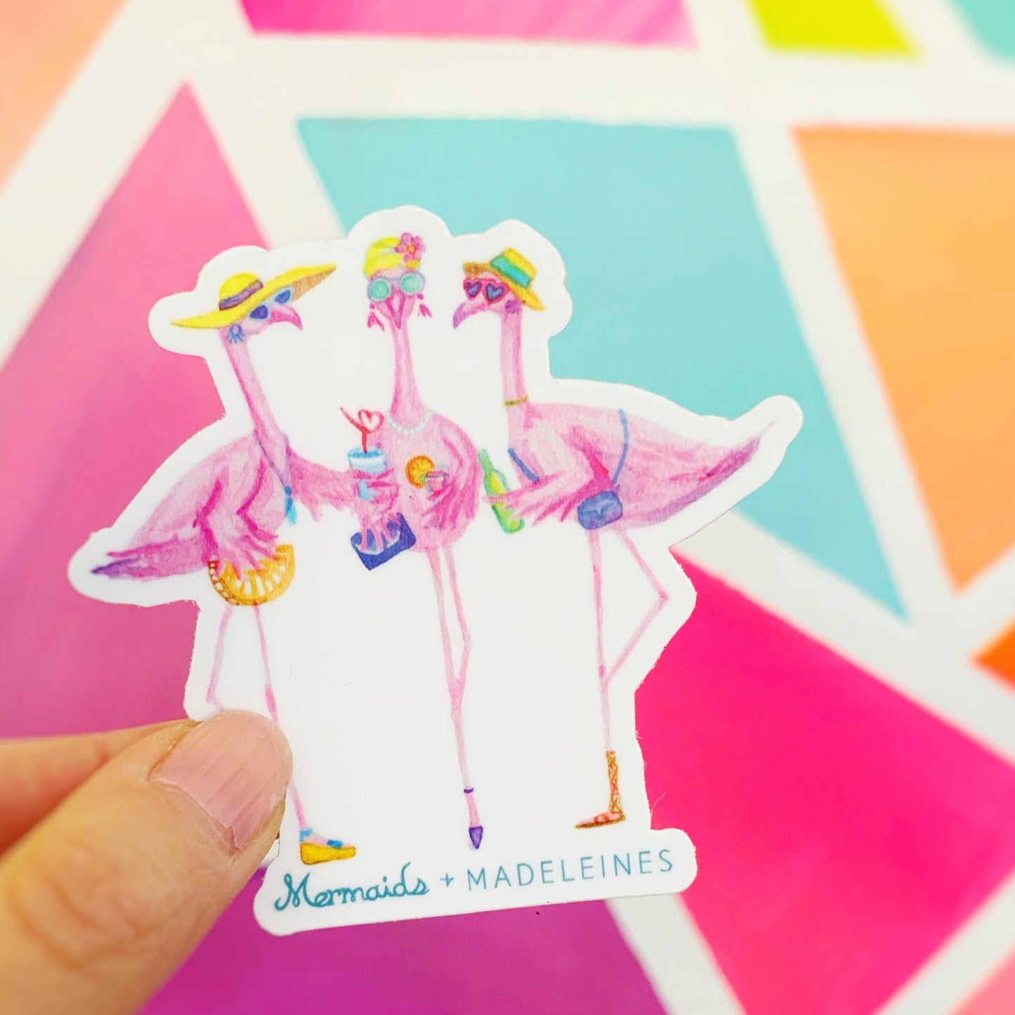 The flamingal sticker is created from original artwork made with acrylic paint and marker its 3 flamingo ladies dressed in summer hats and various footwear. This is a picture of one sticker being held up in front of a bright neon mural
