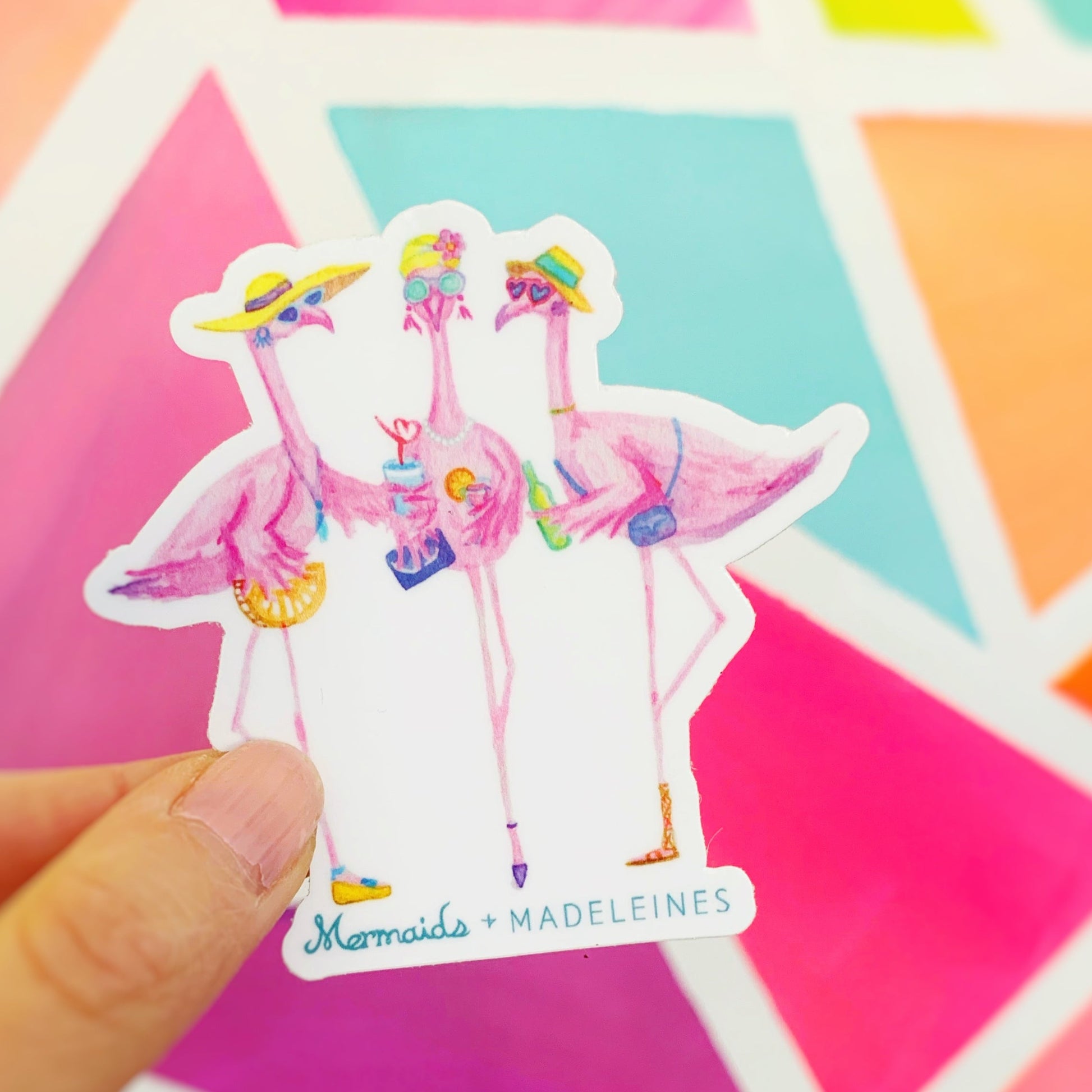 A picture of the Flamingal summer vinyl sticker being held up in front of a bright neon mural. The flamingal sticker is created from original artwork made with acrylic paint and marker its 3 flamingo ladies dressed in summer hats and various footwear