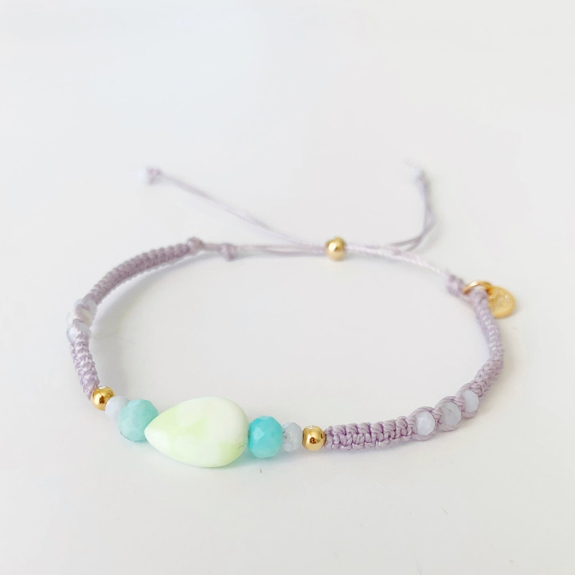 Captiva Macrame bracelet by mermaids and madeleines in color lavender coastal haze. The bracelet has summer color semiprecious beads at the center and a 14k gold slide clasp to adjust the bracelet. this piece is photographed on a white background