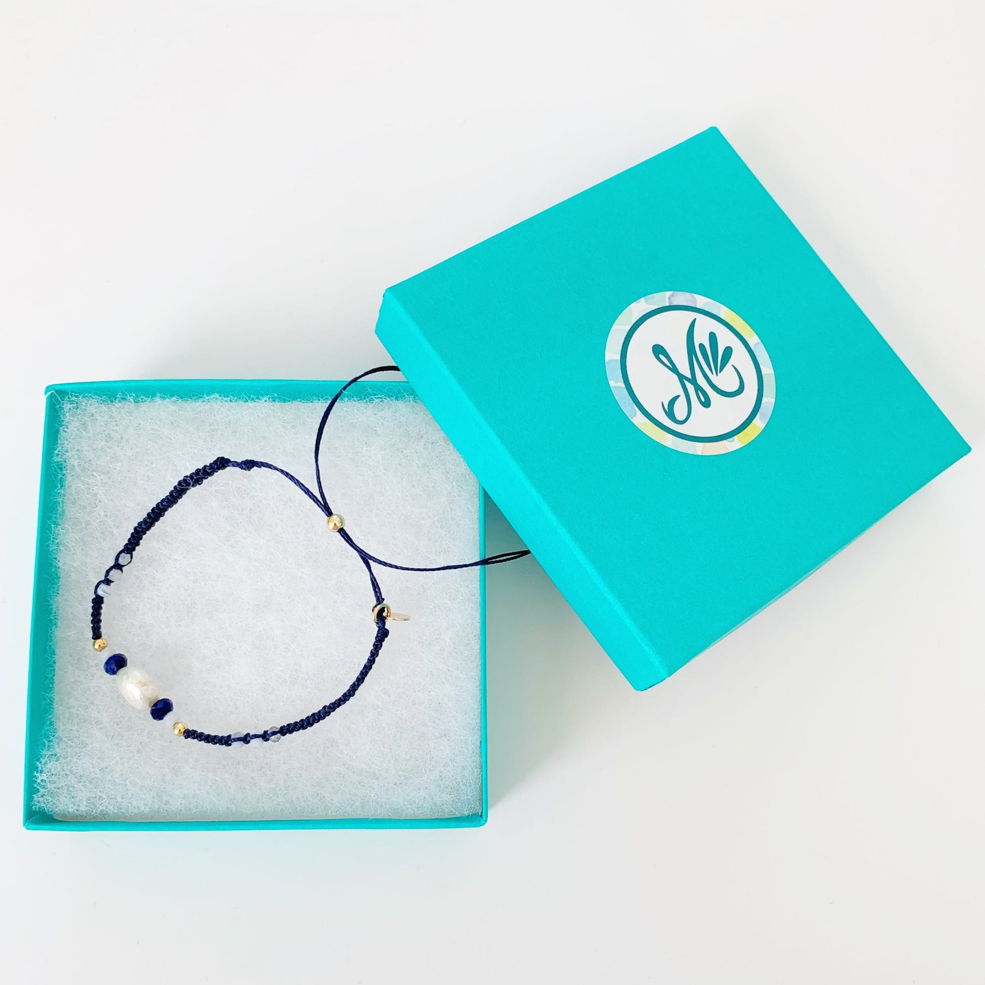 navy blue macrame bracelet pictured in a mermaids and madeleines teal gift box on a white surface