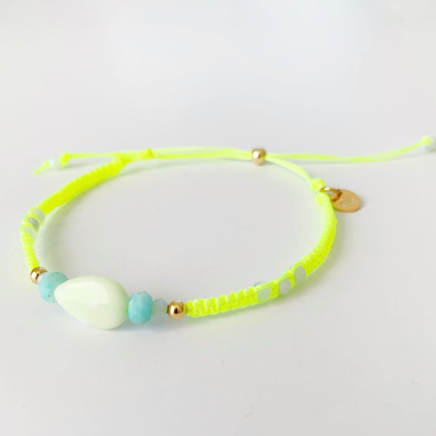 Captiva macrame bracelet by mermaids and madeleines in color sips on the court is a neon yellow bracelet with semiprecious beads at the center and a 14k gold filled slide bead clasp. this bracelet is photographed on a white surface