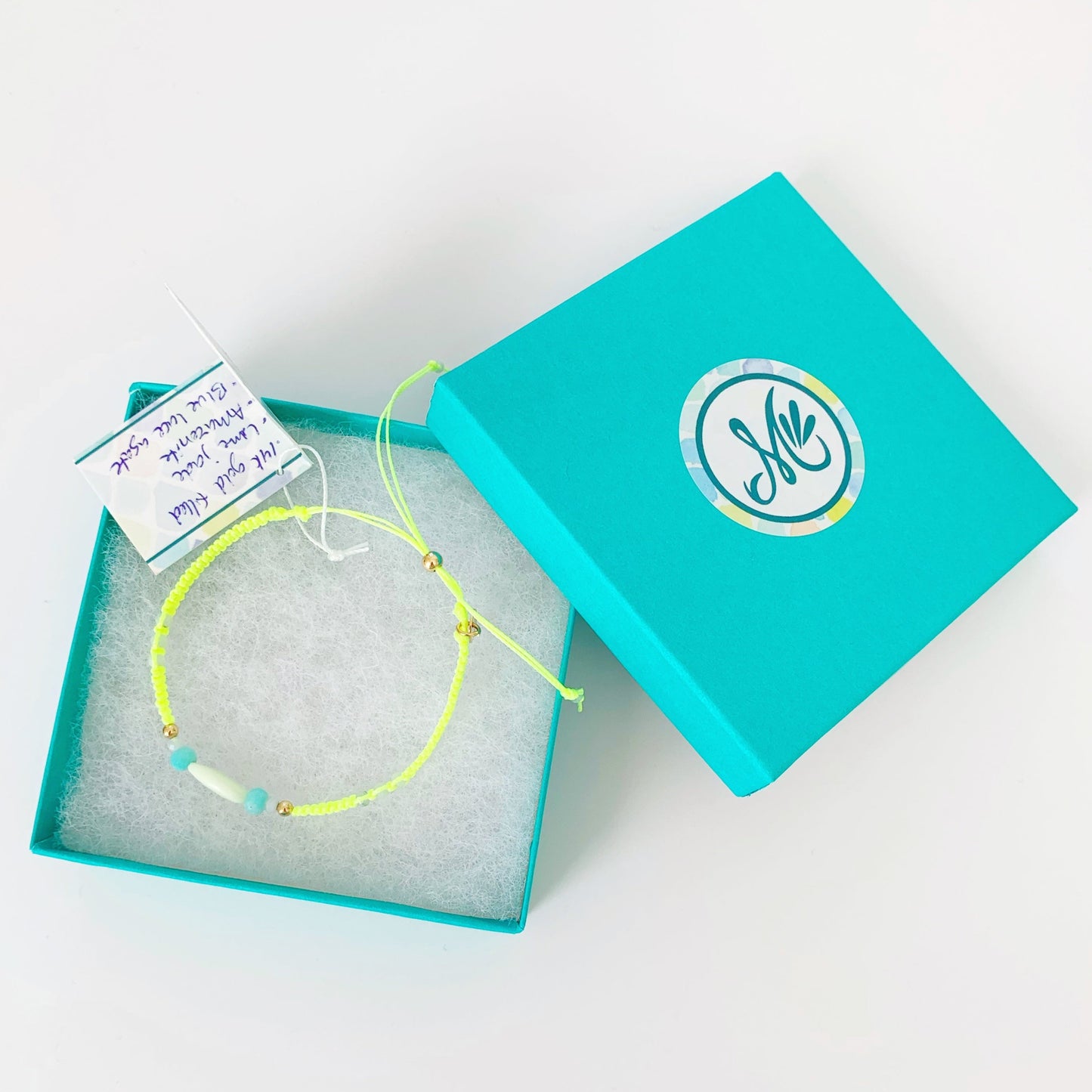 a top view of the neon yellow captiva macrame bracelet in a mermaids and madeleines teal gift box pictured on a white surfae