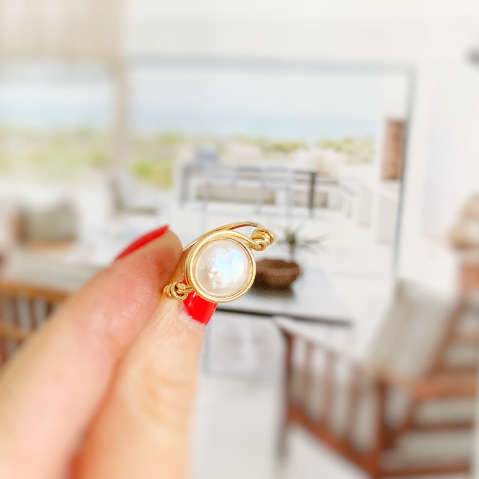 Newport Pearl Ring in 14k gold filled by mermaids and madeleines. this ring is a wire wrapped ring that features a freshwater coin pearl wire wrapped in 14k gold filled wire creating an artful and simple every day ring. this ring is photographed held between fingers in front of a blurred living room scene