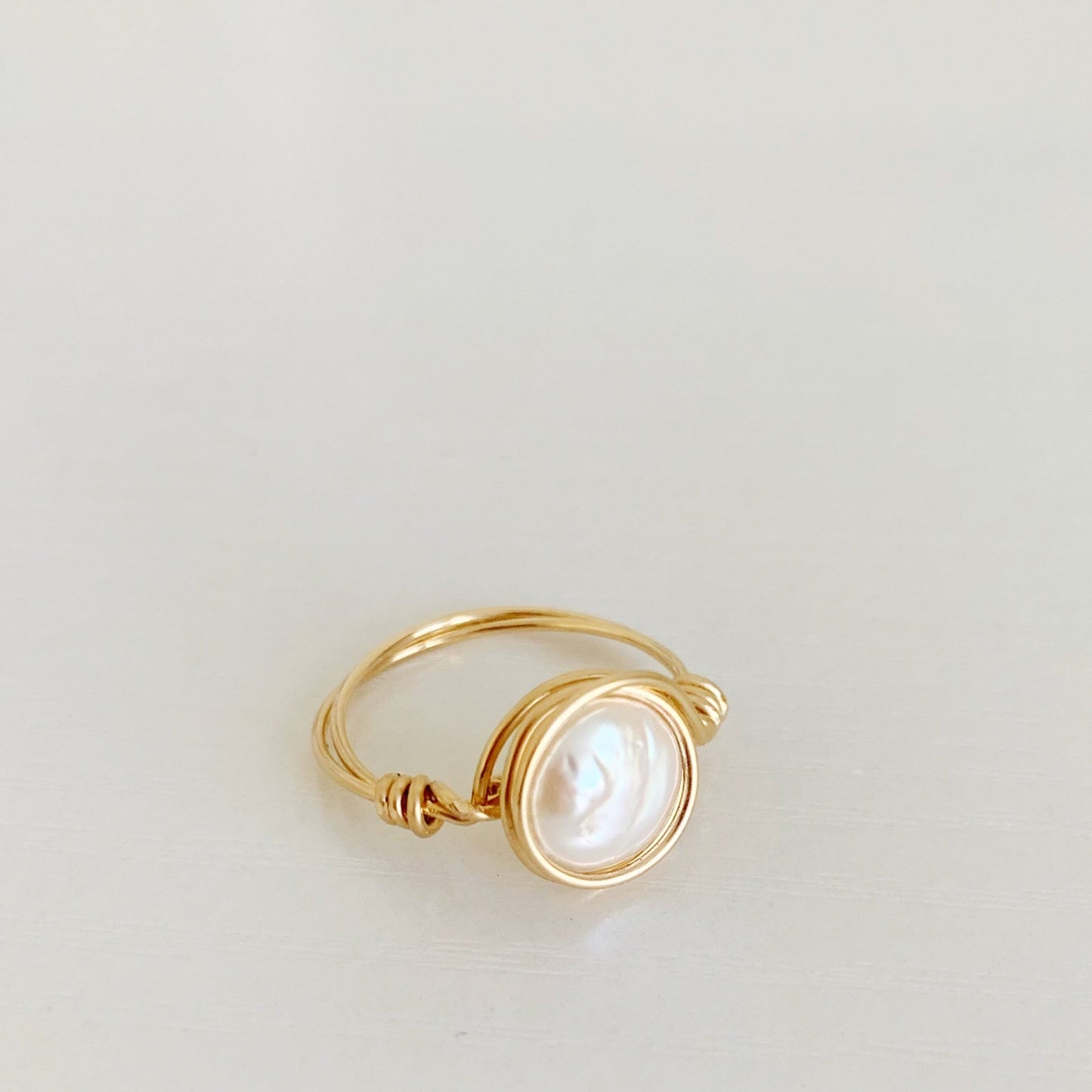 Newport Pearl Ring in 14k gold filled by mermaids and madeleines is a wire wrapped ring that features a freshwater white coin pearl wire wrapped in 14k gold filled wire creating an artful and simple ring. this one is photographed at an angle on a white surface