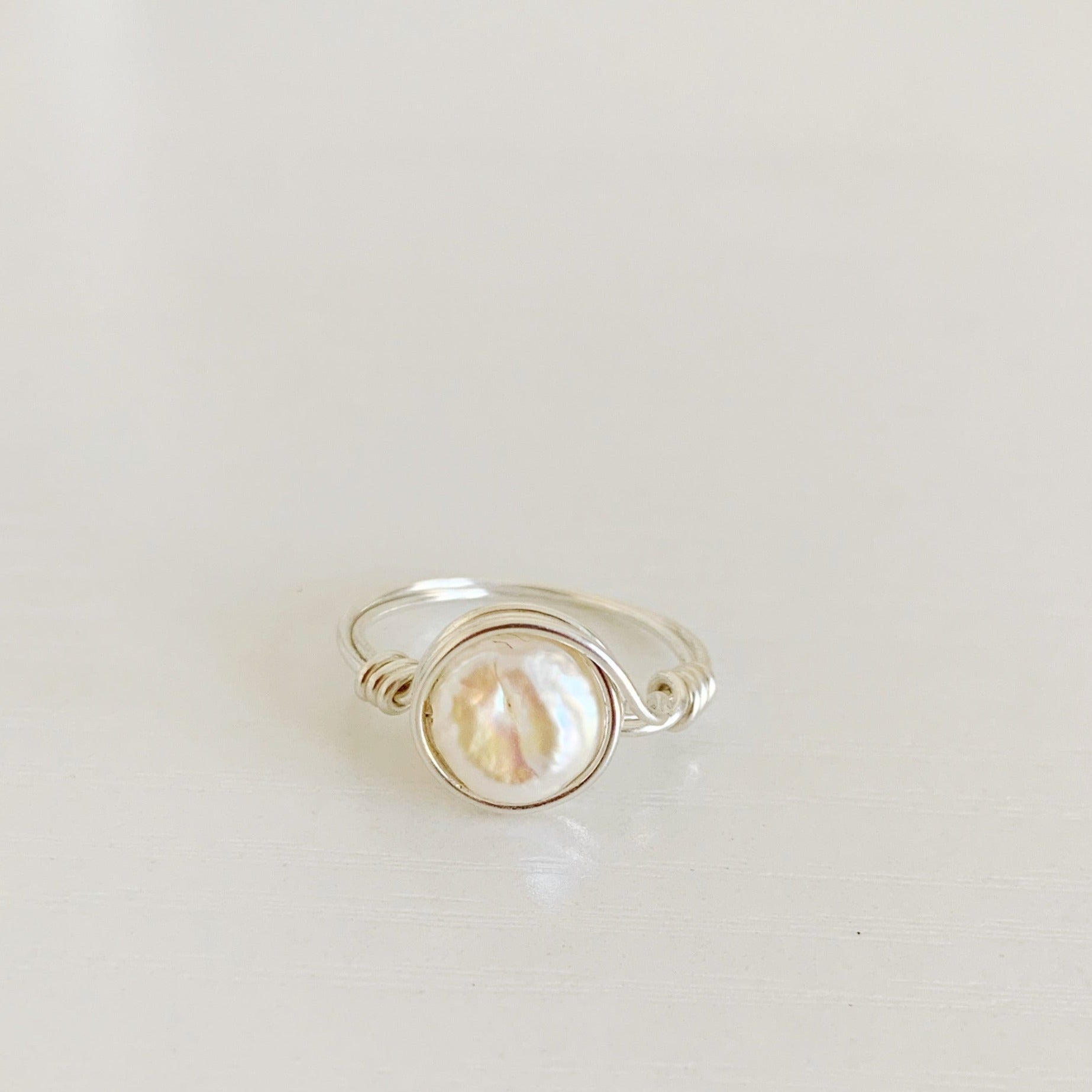 Newport Pearl Ring in sterling silver by mermaids and madeleines. this ring features a freshwater coin pearl and sterling silver wire. The ring is a wire wrap style making it simple and artful. this ring is photographed from a front view on a white surface