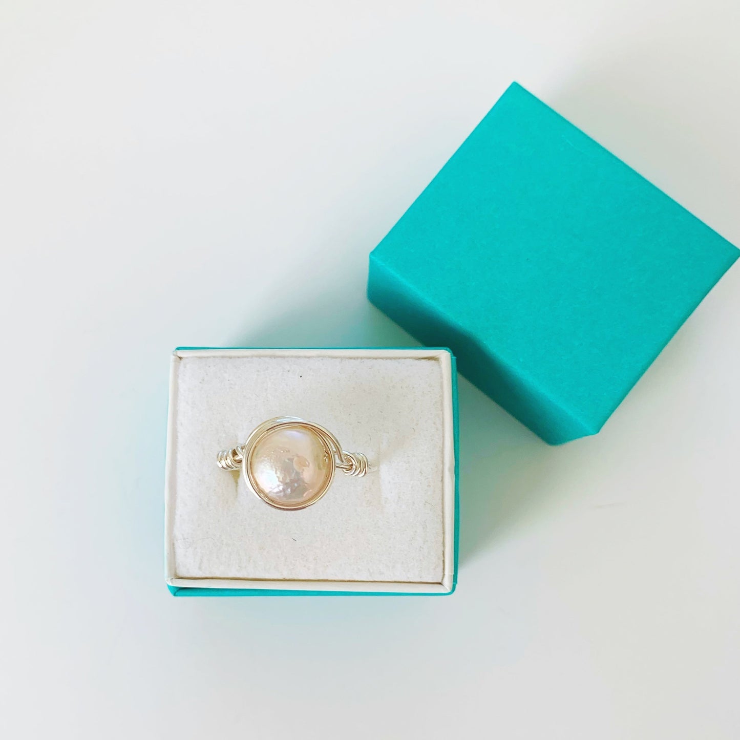 The newport pearl wire wrapped ring in sterling silver pictured in a teal ring box on a white surface