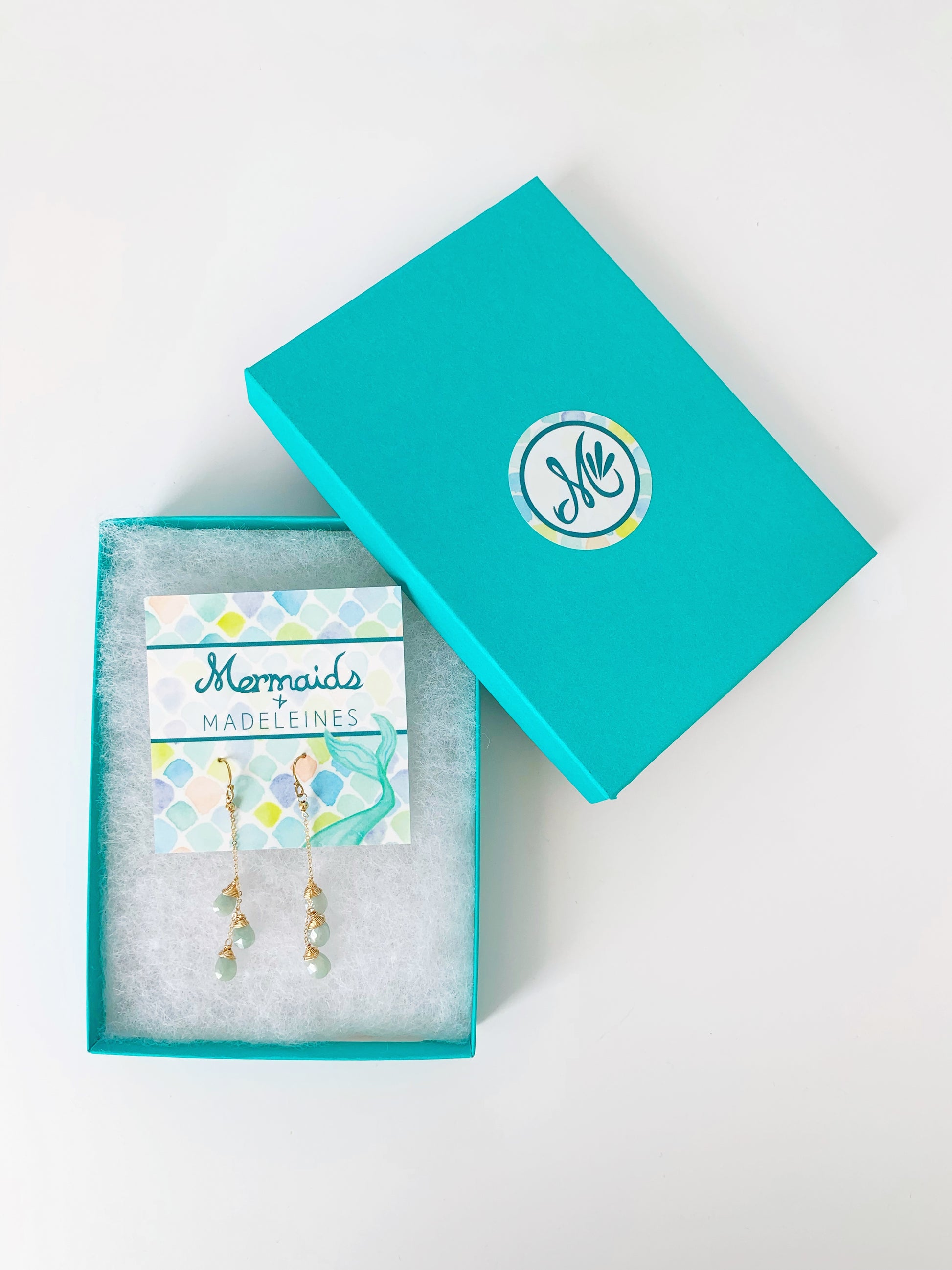 A picture of the 14k gold filled raindrop aquamarine earrings in a teal gift box on a white surface